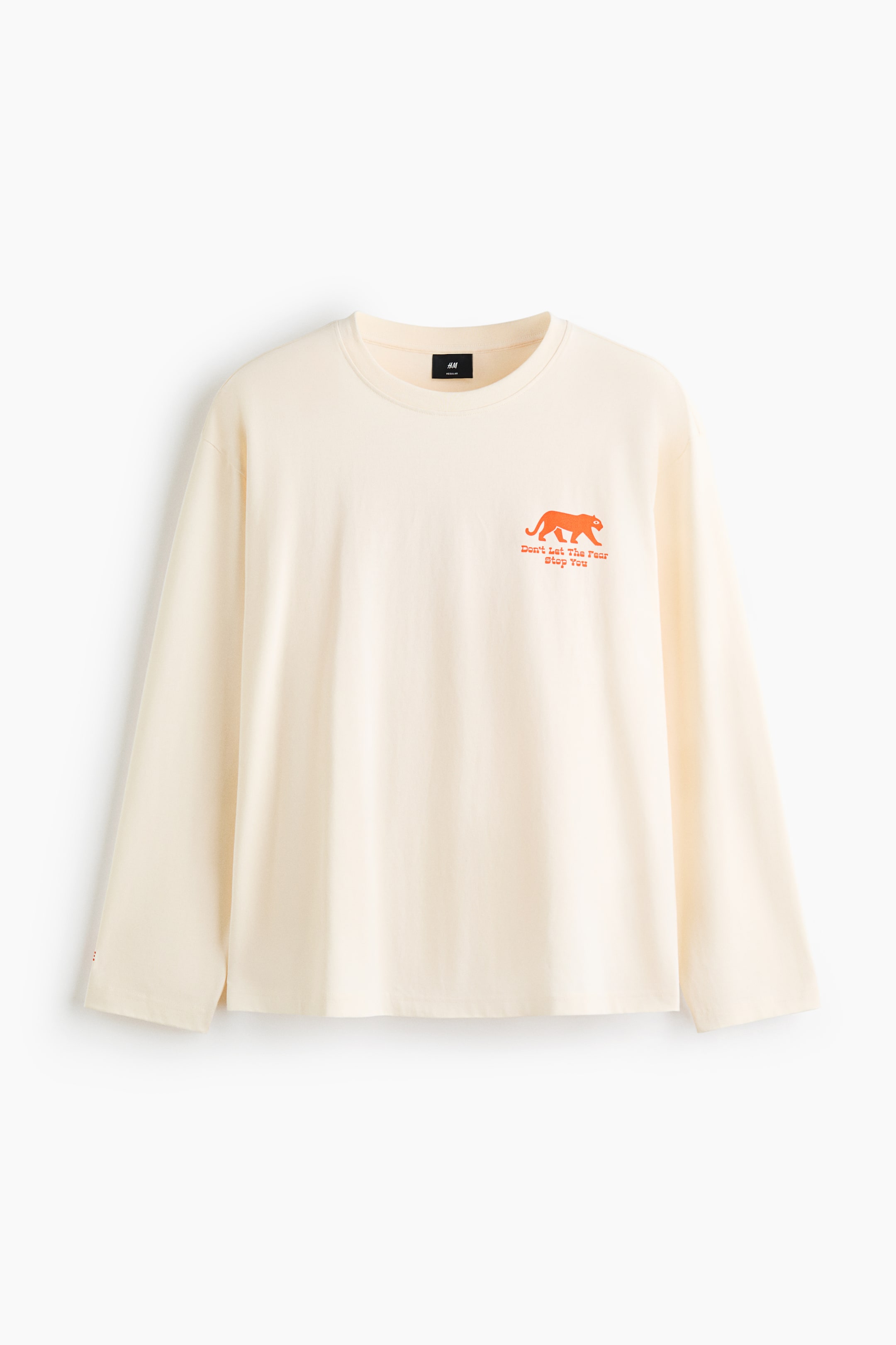 View larger image: A cream-coloured, long-sleeve T-shirt is displayed from a front-facing perspective, featuring a ribbed crew neck, dropped shoulders, and a straight hem. A small orange graphic of a walking panther with the text "Don't Let The Fear Stop You" is printed on the left chest.