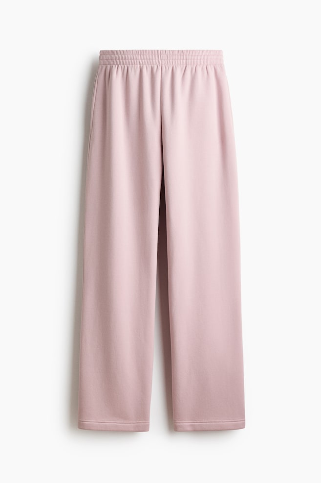 Light pink sweatpants are displaying an elasticated smocking at the waist and visible side pockets. They are featuring straight legs and are presented from a front angle. - 1