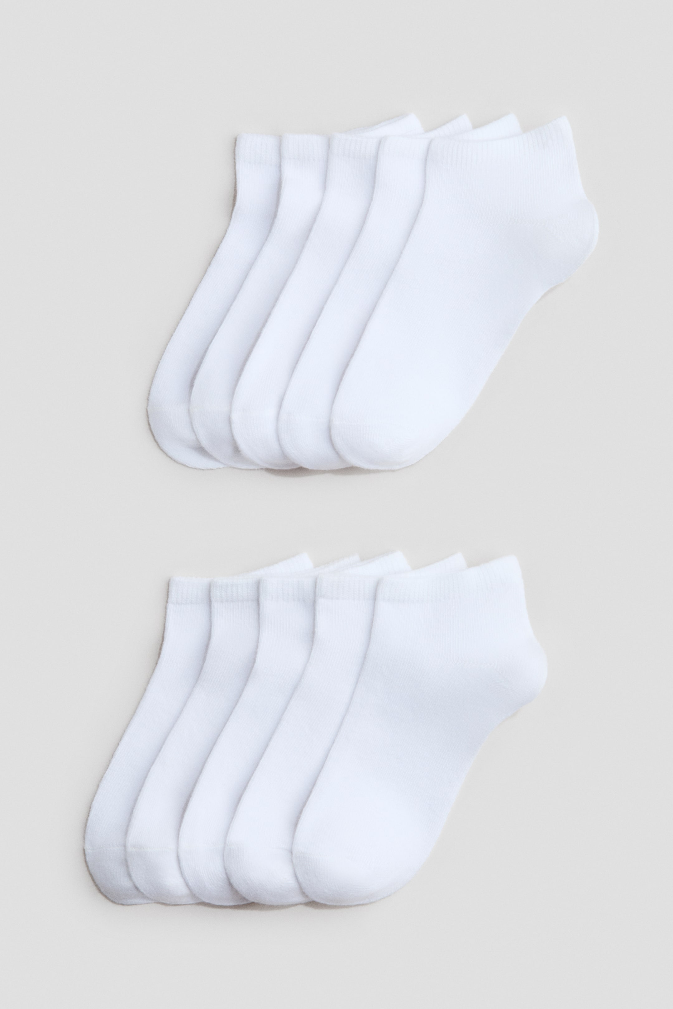 View larger image: White trainer socks are displayed in two neat rows of five, each sock slightly overlapping the next. They boast a fine-knit texture and elasticated cuffs at the tops.