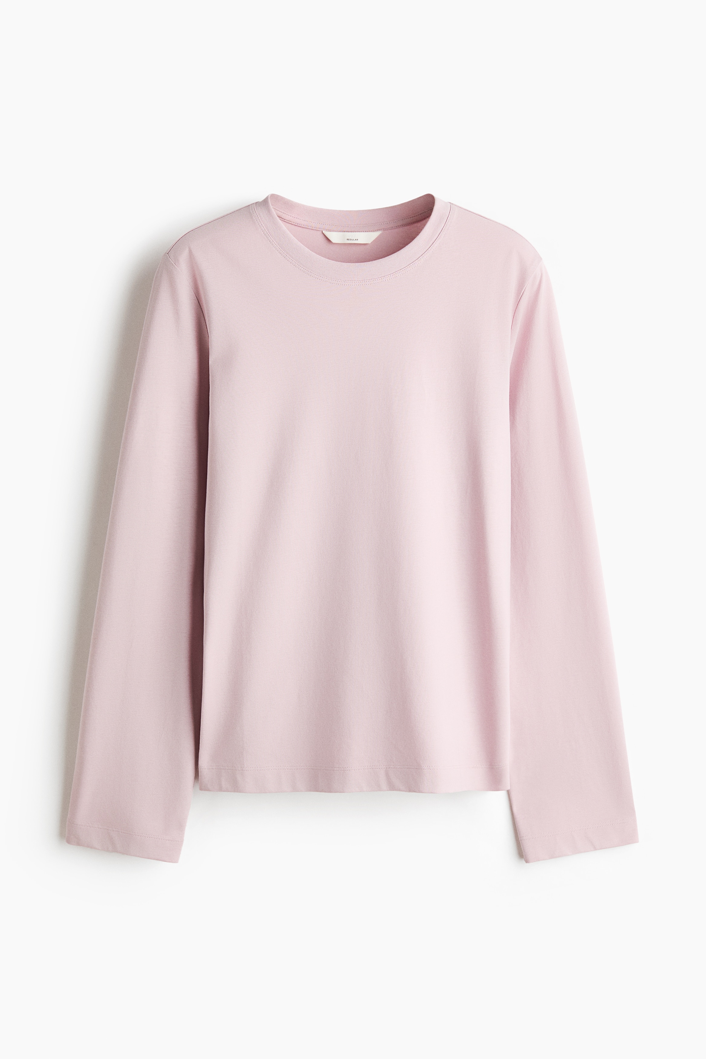A light pink, long-sleeved crew-neck top is being worn by the model, styled with a striped pink and dark burgundy jumper tied around the waist. The outfit is completed with dark, relaxed-fit trousers.