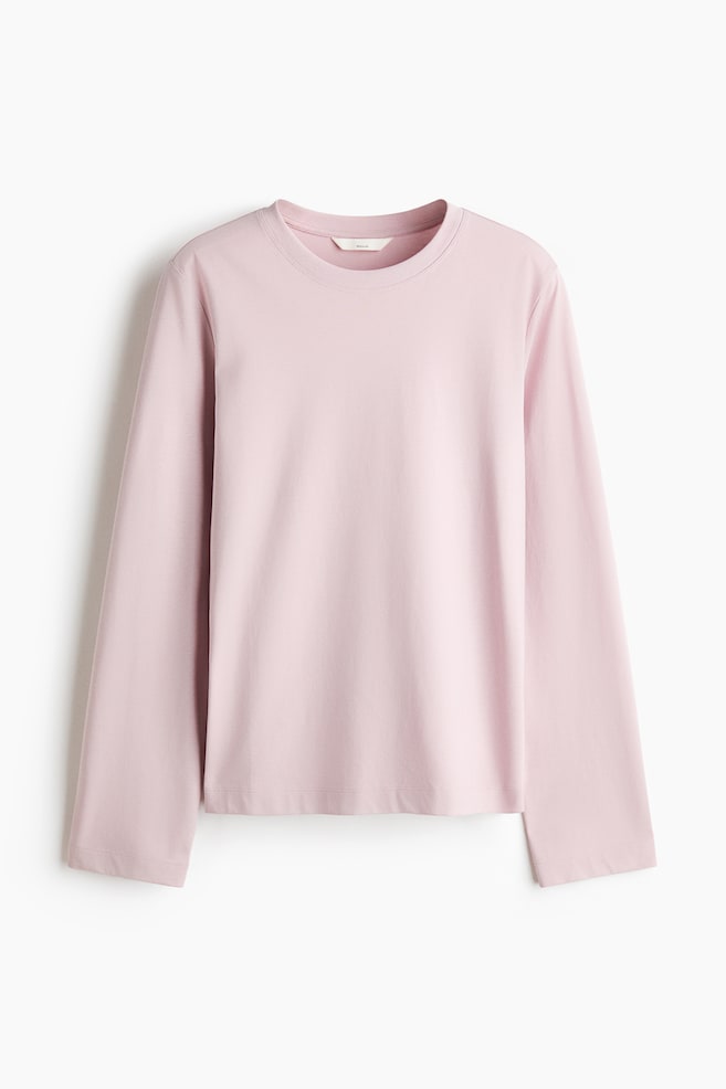 Un top in jersey di cotone rosa chiaro Ã¨ appeso frontalmente, con scollo rotondo rifinito a coste e maniche lunghe e dritte con polsini a finitura pulita. - 1
