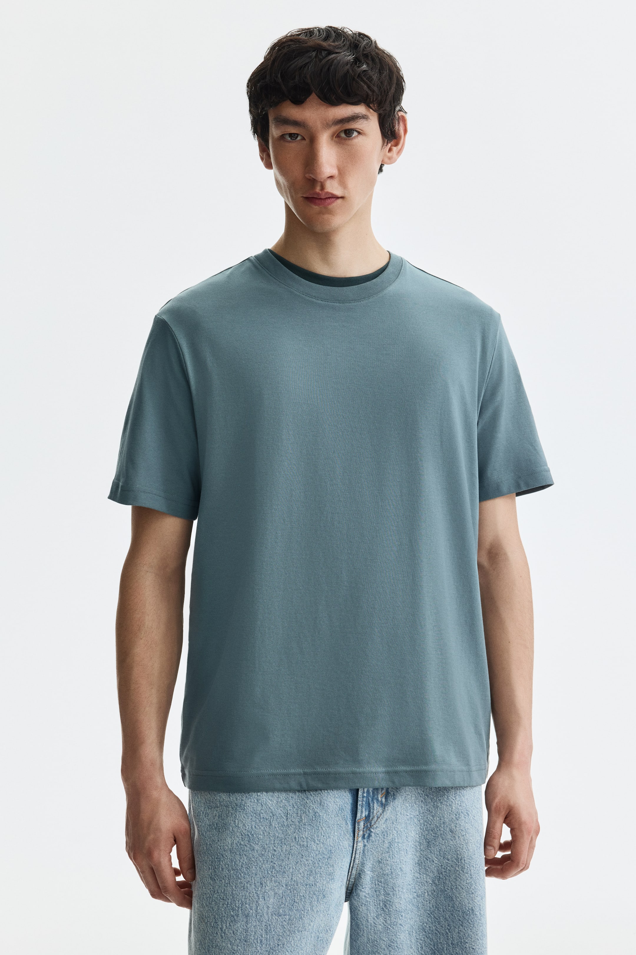 View larger image: A teal short-sleeve t-shirt is showcased from the front, featuring a crew neck with a darker undershirt visible at the neckline. It displays a relaxed fit and a straight hem.