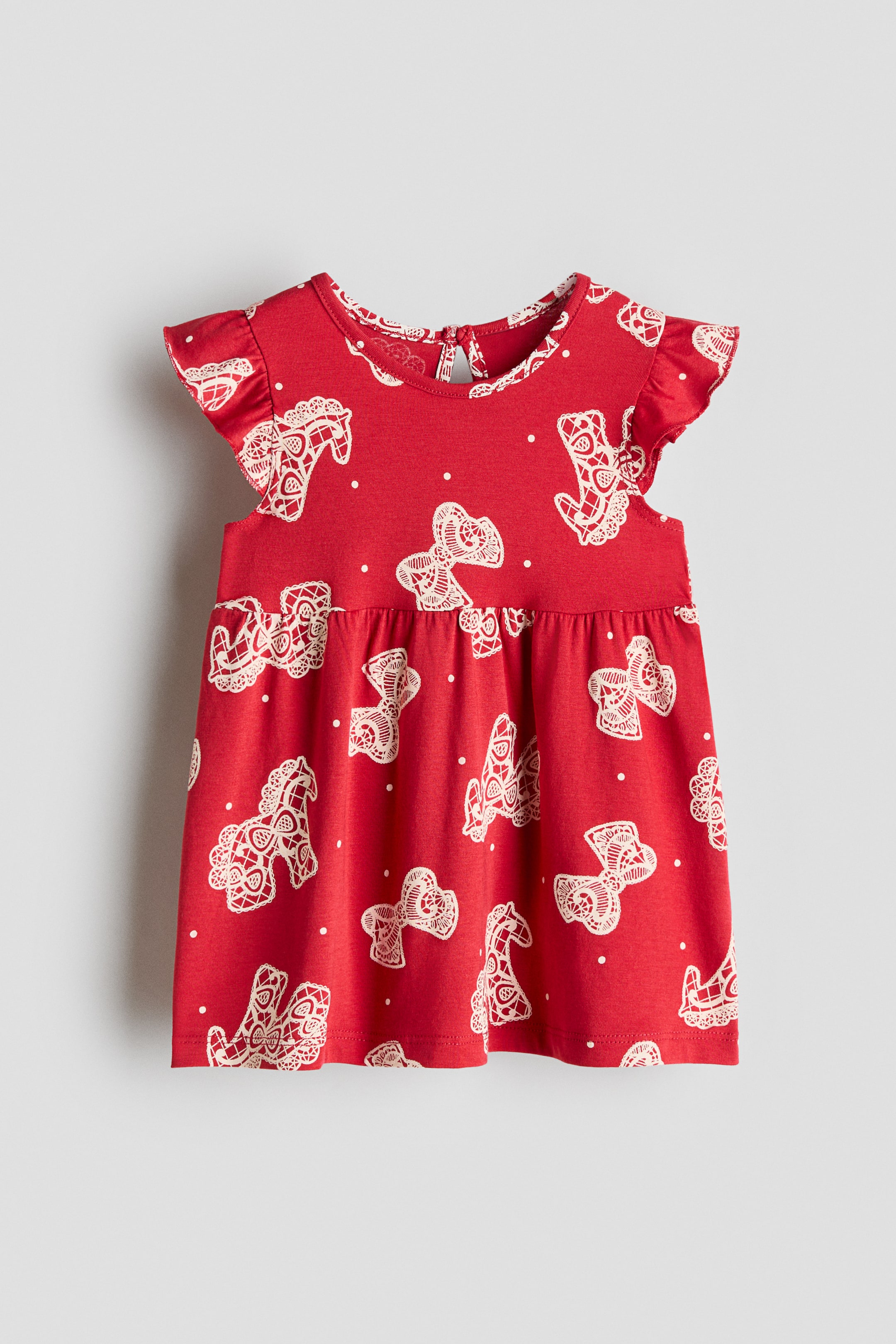 View larger image: A red dress is displaying a pattern of white lace-like horses and small white polka dots. It is featuring a round neckline, ruffled cap sleeves, and a gathered waistline forming a flared skirt.