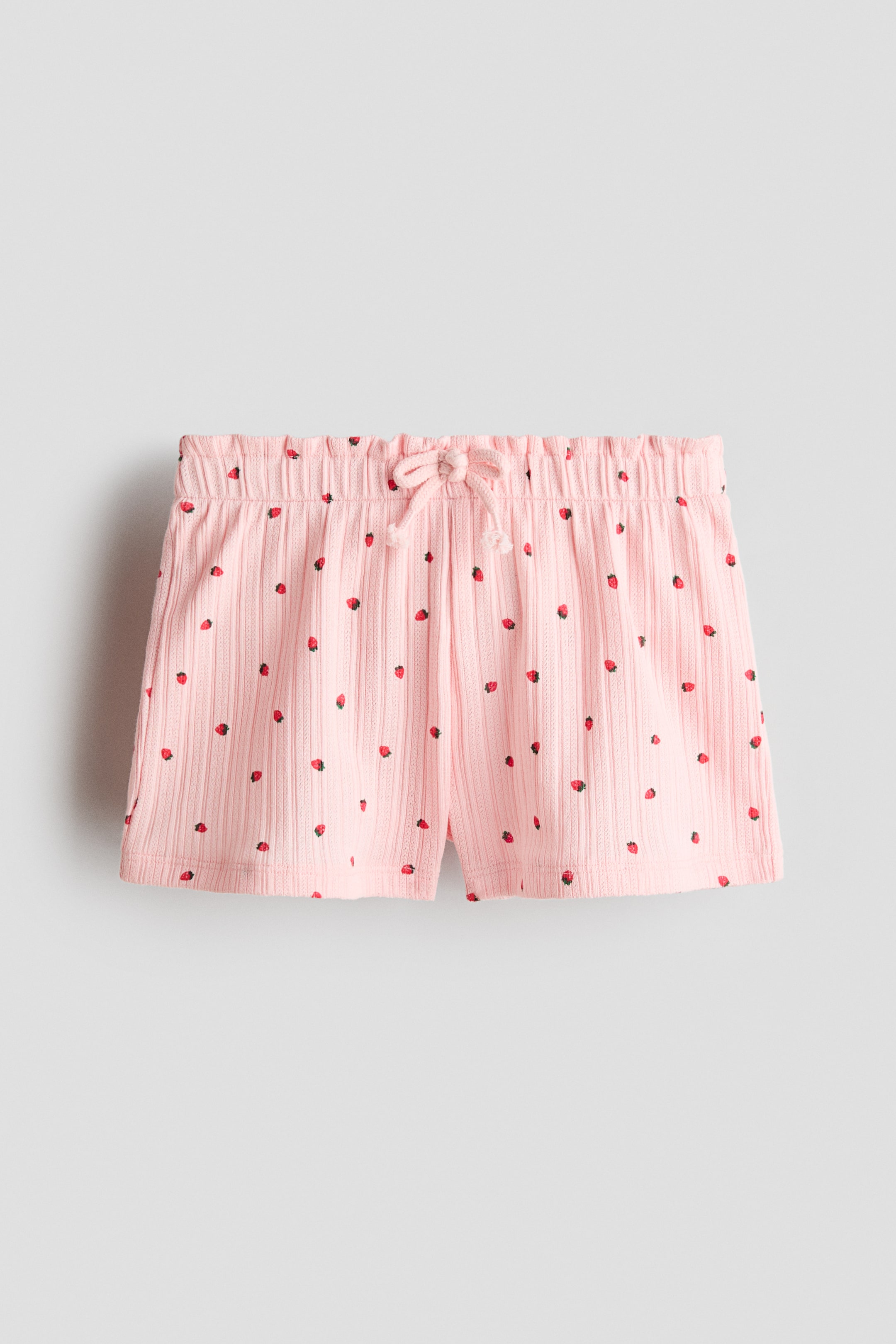 Vis større bilde: Rosa shorts med ribbestrikket tekstur og et heldekkende jordbærmønster. Shortsene har en elastisk linning og en rosa snor som er knyttet i en sløyfe foran.