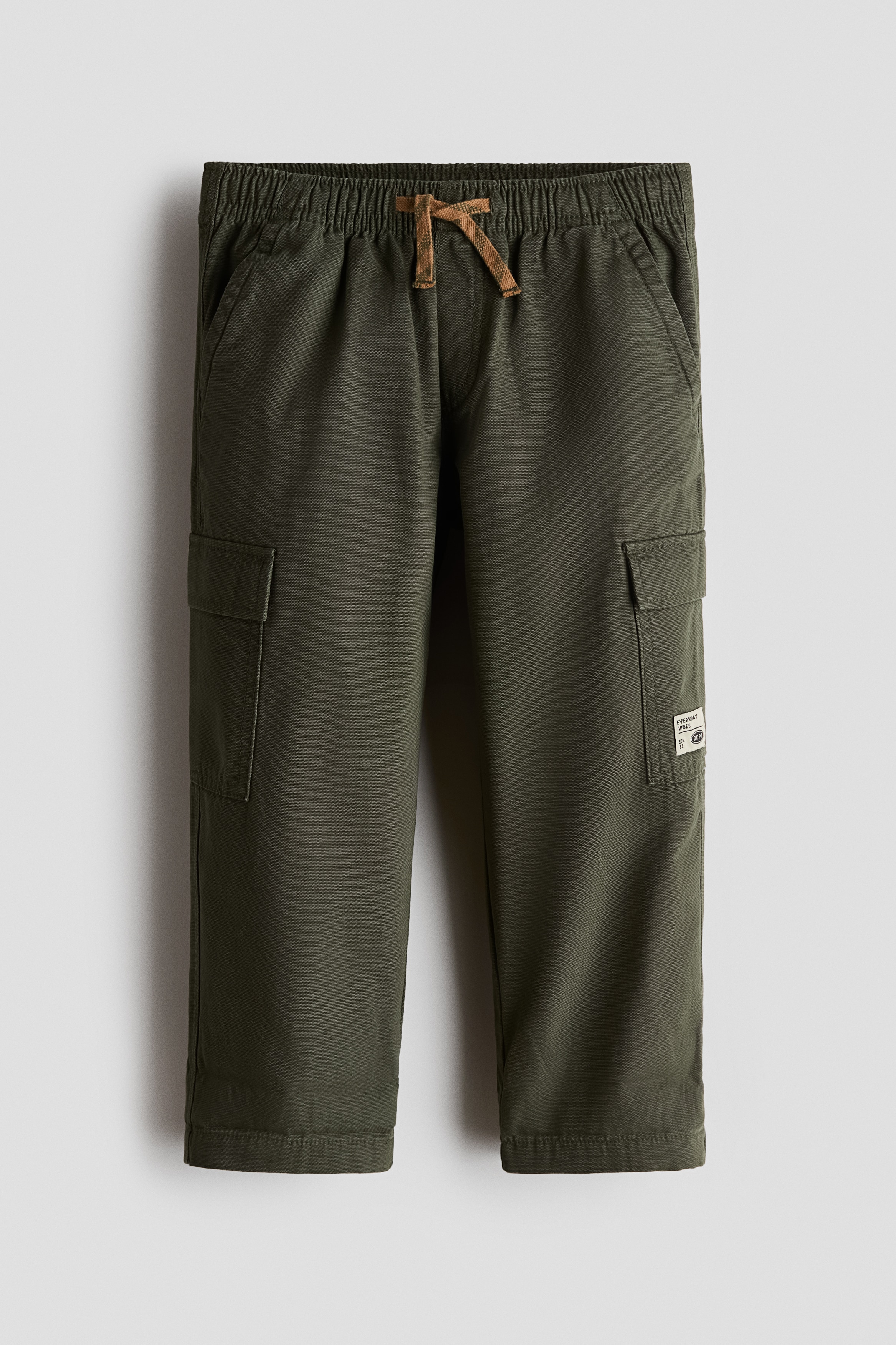Quần jogger cargo bằng vải canvas cotton mà u xanh lá Äáºm ÄÆ°á»£c chụp á» góc nghiêng bên hông, là m ná»i báºt phom dáng rá»ng và thiết kế tiá»n Ãch. Quần có túi bên chéo và má»t túi á»p có nắp á» bên á»ng quần.