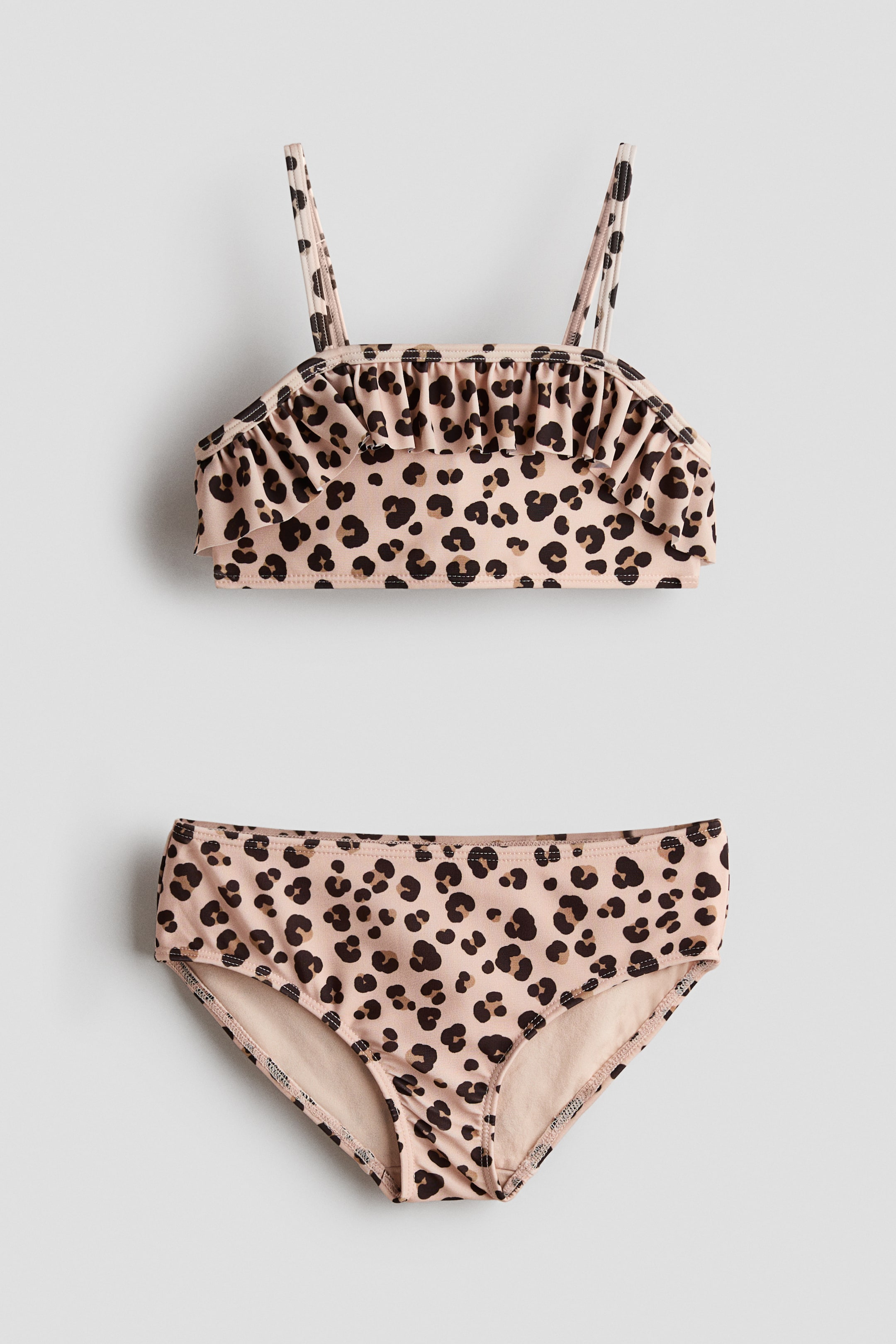 Grösseres Bild ansehen: Ein Leopardenmuster-Bikini-Set wird von vorne präsentiert, mit einem Oberteil, das einen Rüschenbesatz und elastische Träger hat. Die passenden Unterteile zeigen ein hellbeiges Futter entlang der Beinausschnitte.
