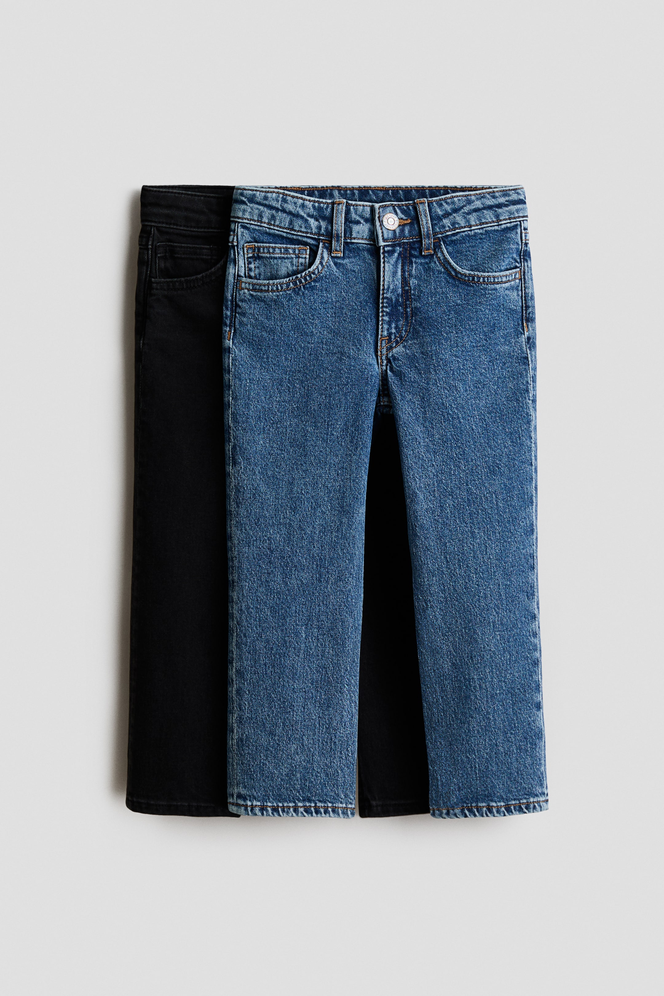 Voir une image plus grande: Deux paires de jeans en denim à 5 poches sont présentées de face, avec une paire bleue superposée sur une paire noire, toutes deux affichant une coupe décontractée au niveau des hanches, des cuisses et des jambes, et dotées d'une ceinture avec passants pour ceinture, d'une fermeture à bouton et d'une braguette zippée.