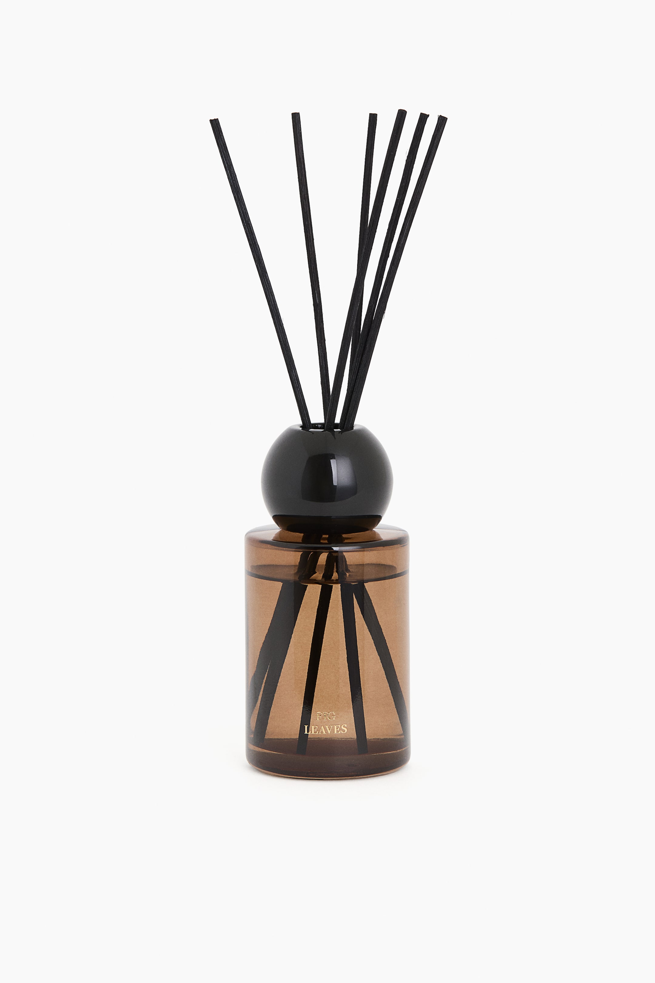 View larger image: A scented oil diffuser consists of a cylindrical amber-tinted glass bottle filled with liquid, with multiple black diffuser reeds extending upwards from a glossy black spherical cap. Small gold text "P&G LEAVES" is visible on the front of the bottle.