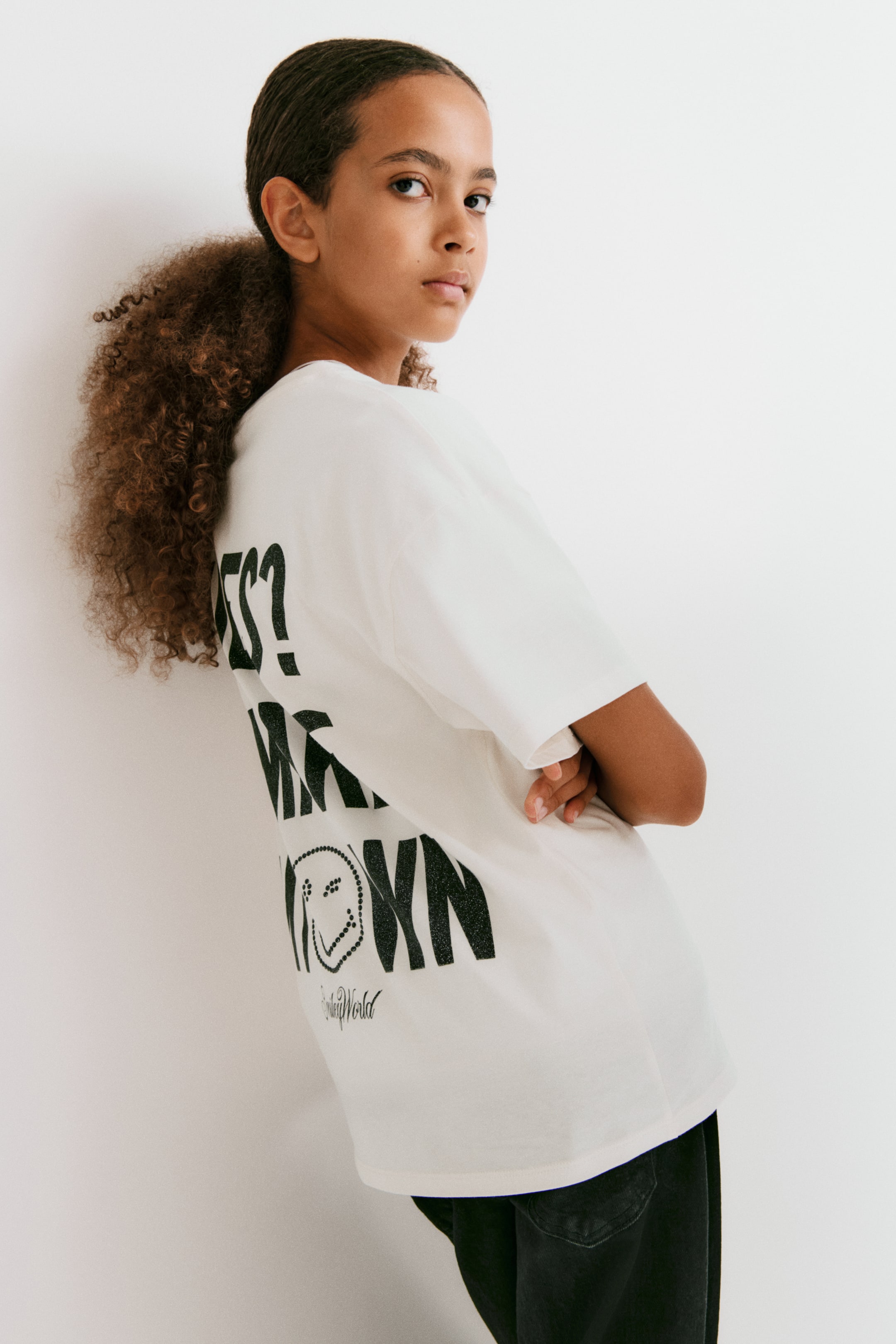 Ampliar la imagen: Playera de jersey de algodón suave con estampado, mostrada por la parte trasera, que presenta un gran estampado gráfico negro con texto en negritas y una carita sonriente de puntos. Cuenta con hombros ligeramente caídos.