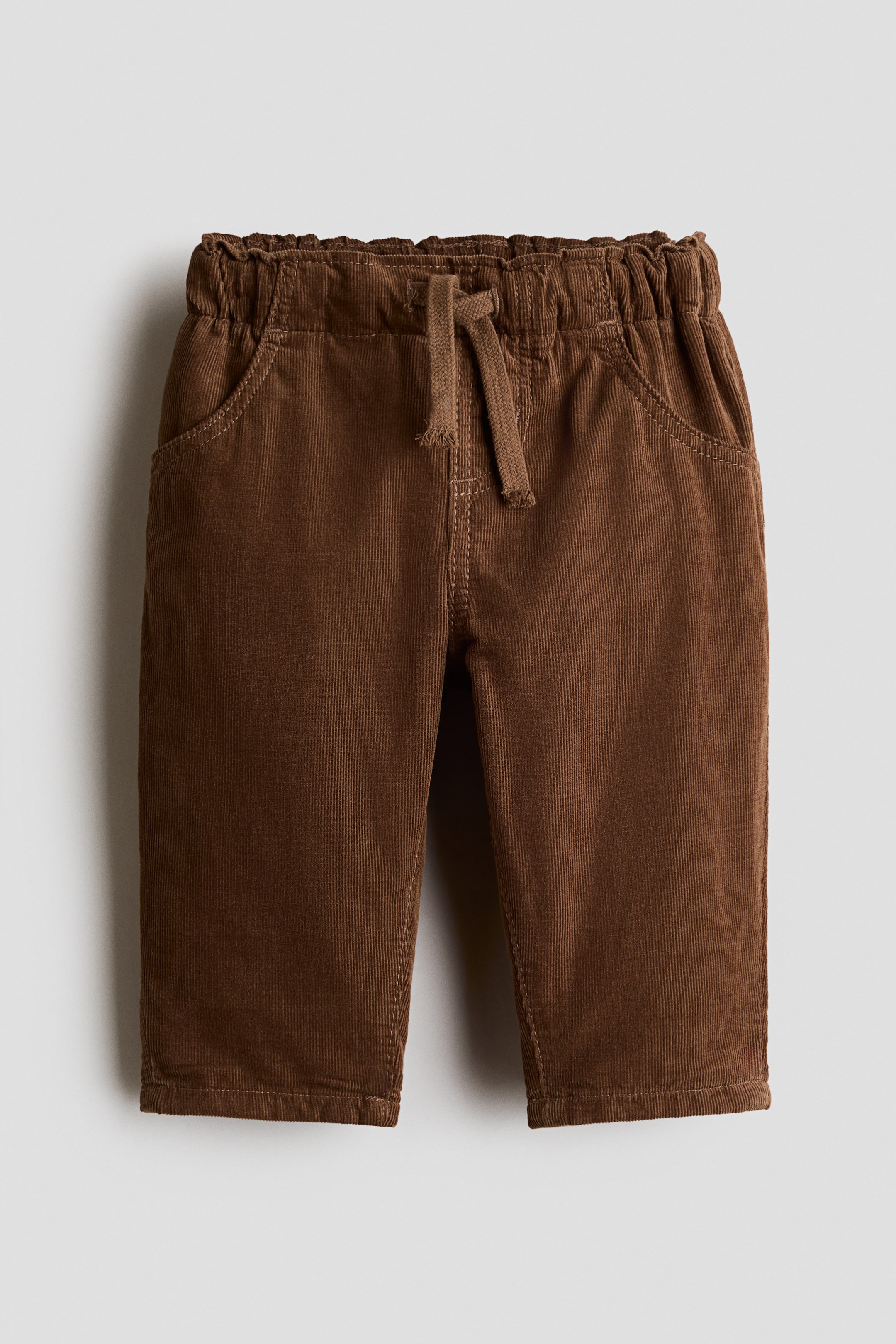 View larger image: Brown corduroy trousers are shown from the front, featuring an elasticated, ruched waistband with a drawstring and two curved front slash pockets.