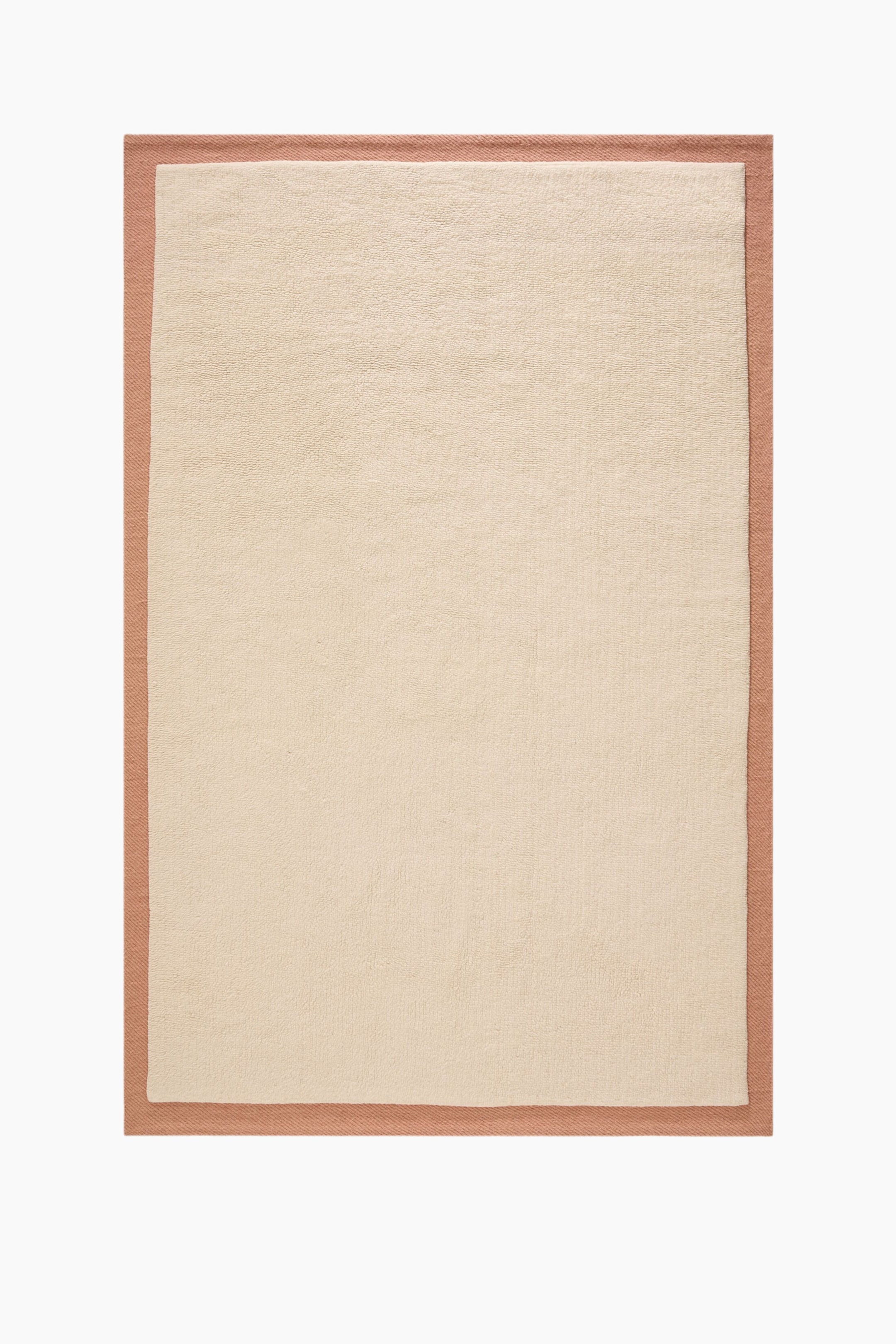 Ver imagem maior: Um tapete retangular apresenta um centro felpudo de cor creme com uma textura de pêlo cortado e macio. Este centro é emoldurado por uma borda em tom de salmão, que exibe uma textura tecida diagonal distinta, criando um design em camadas.