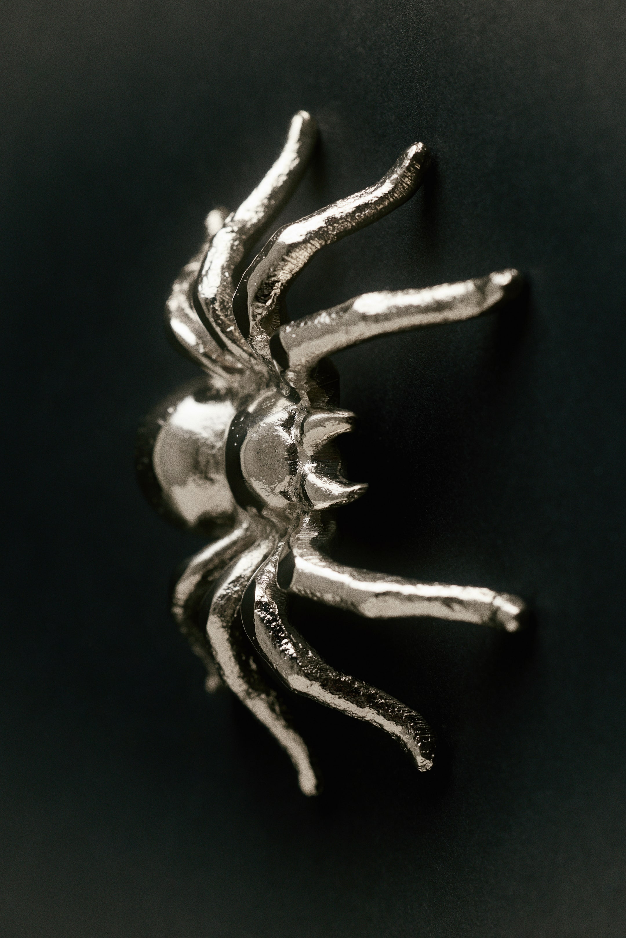 View larger image: A spider-shaped Halloween decoration crafted from textured, metallic silver aluminum is displayed from a side-profile angle. The product features curved legs and a shiny, slightly hammered surface finish.