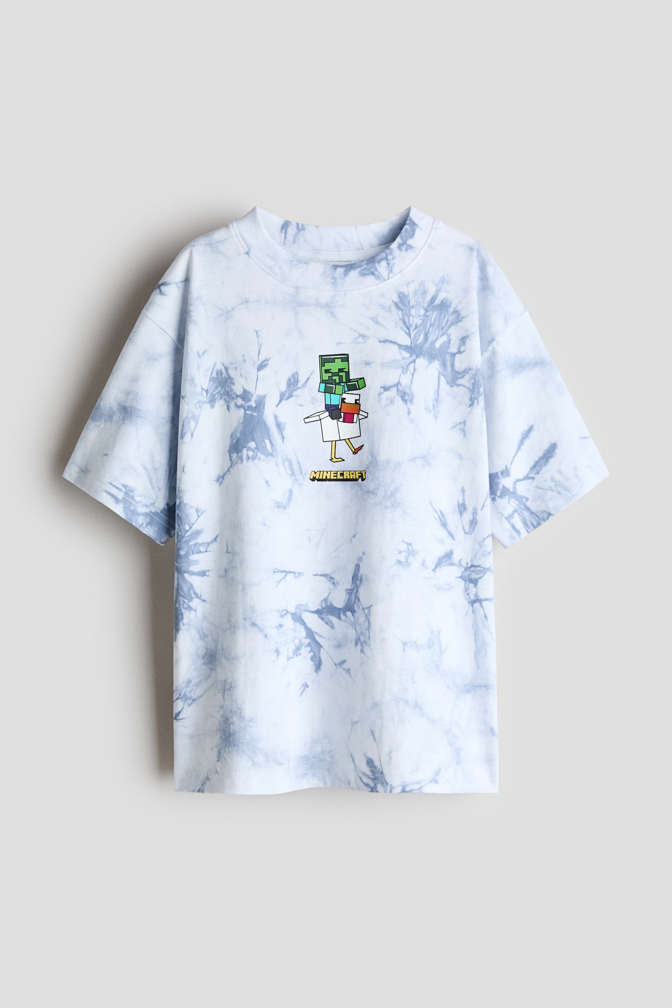 Ver imagen más grande: La camiseta se presenta por delante, mostrando un patrón de teñido anudado en blanco y azul claro y un estampado gráfico de un personaje pixelado verde montando un pollo blanco con el texto "MINECRAFT" debajo. Cuenta con un cuello redondo acanalado, un ajuste holgado y hombros caídos.