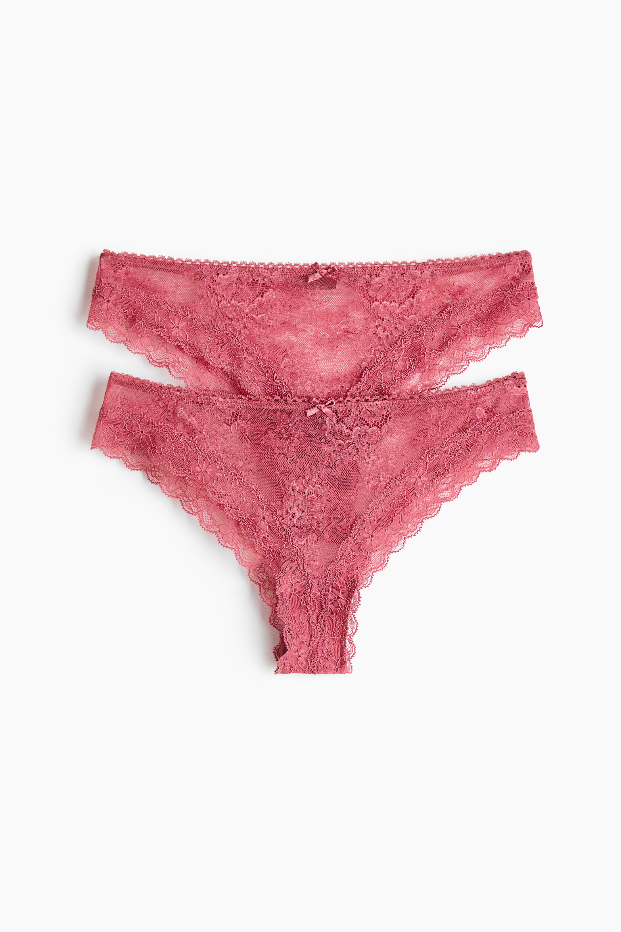 Größeres Bild anzeigen: Zwei rosa Spitzenstrings liegen flach, mit der Vorderseite nach oben. Jeder String zeigt ein florales Spitzenmuster, gewellte Kanten und eine kleine Schleife an der Vorderseite.