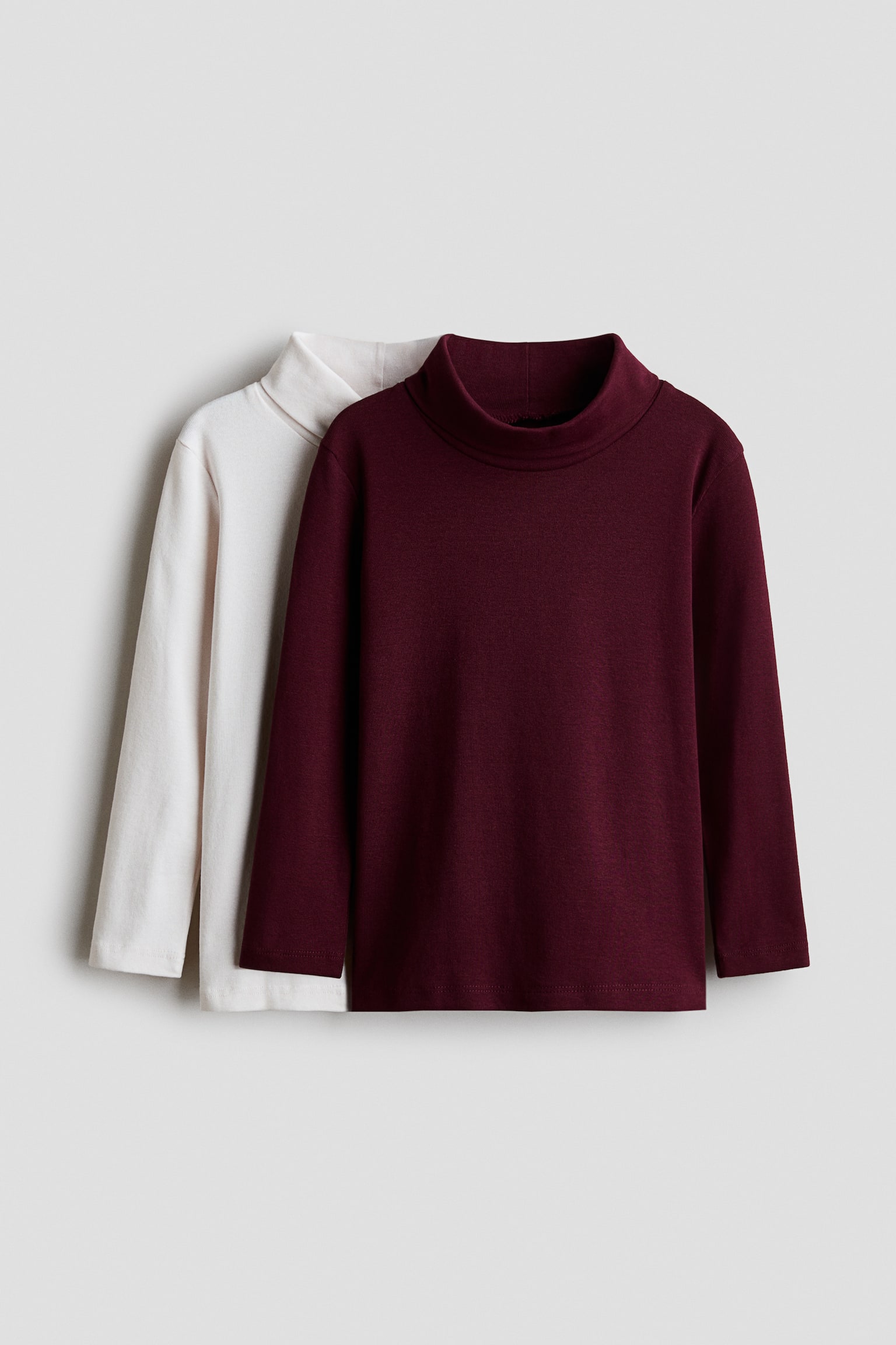 Due top a maniche lunghe con collo alto finto sono mostrati frontalmente, con un top bordeaux sovrapposto davanti a un top bianco sporco. Entrambi i top presentano un colletto alto finto rialzato, maniche lunghe e un orlo dritto.
