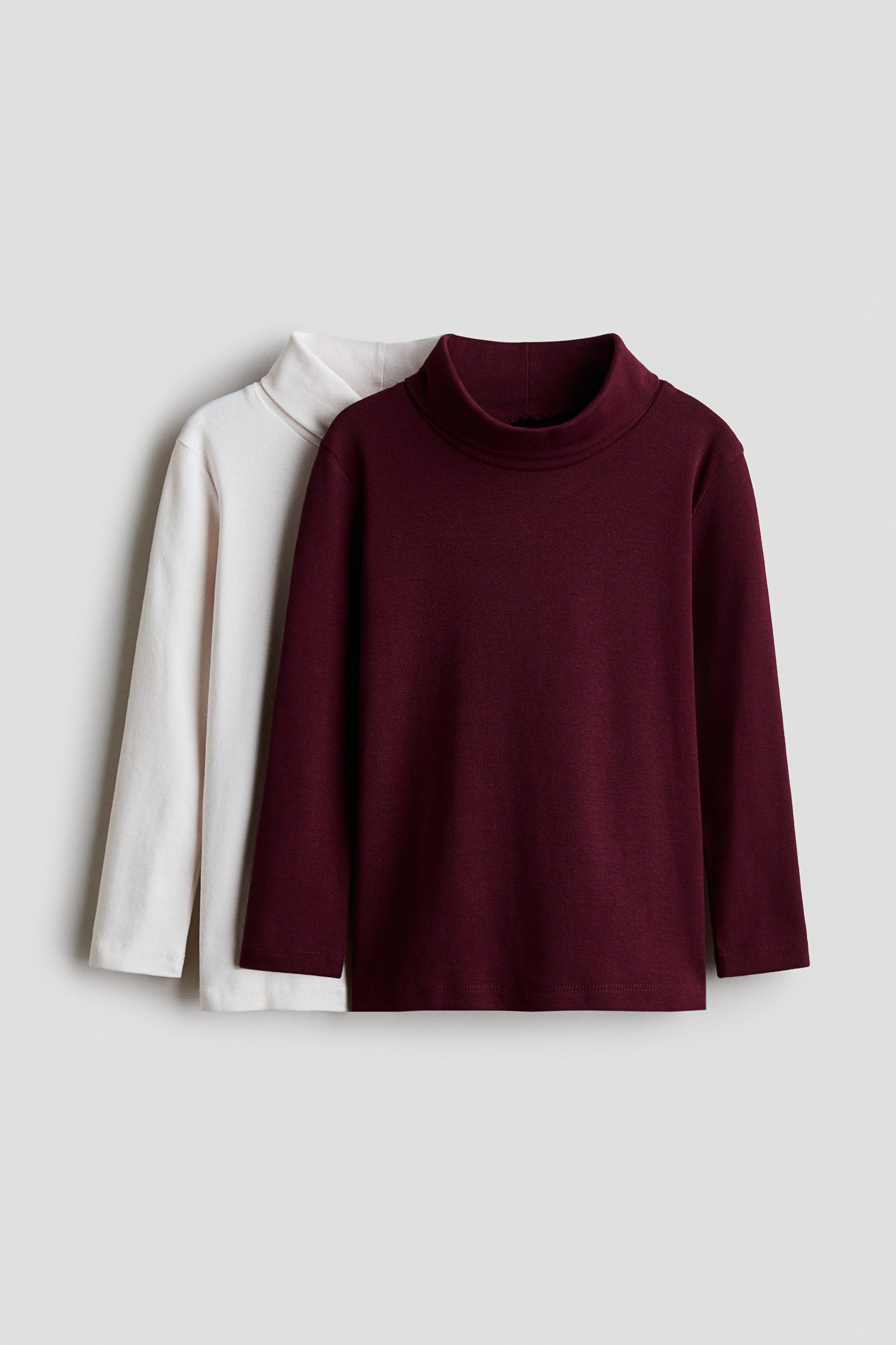 View larger image: Two long-sleeve mock-neck tops are shown from the front, with a burgundy top layered in front of an off-white top. Both tops feature a raised mock-neck collar, long sleeves, and a straight hem.