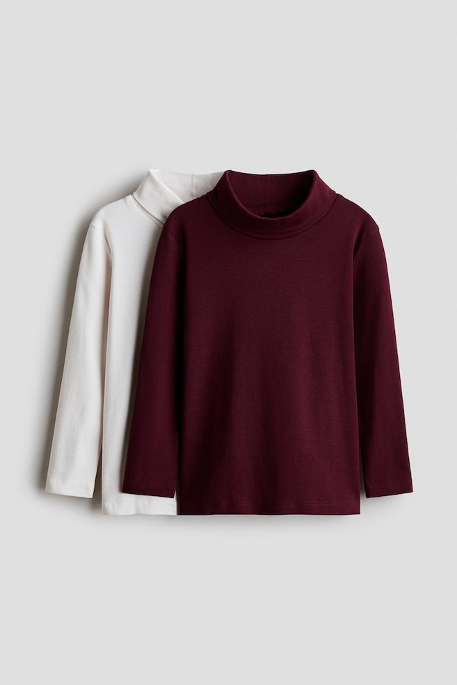 Two long-sleeve mock-neck tops are shown from the front, with a burgundy top layered in front of an off-white top. Both tops feature a raised mock-neck collar, long sleeves, and a straight hem. - 1