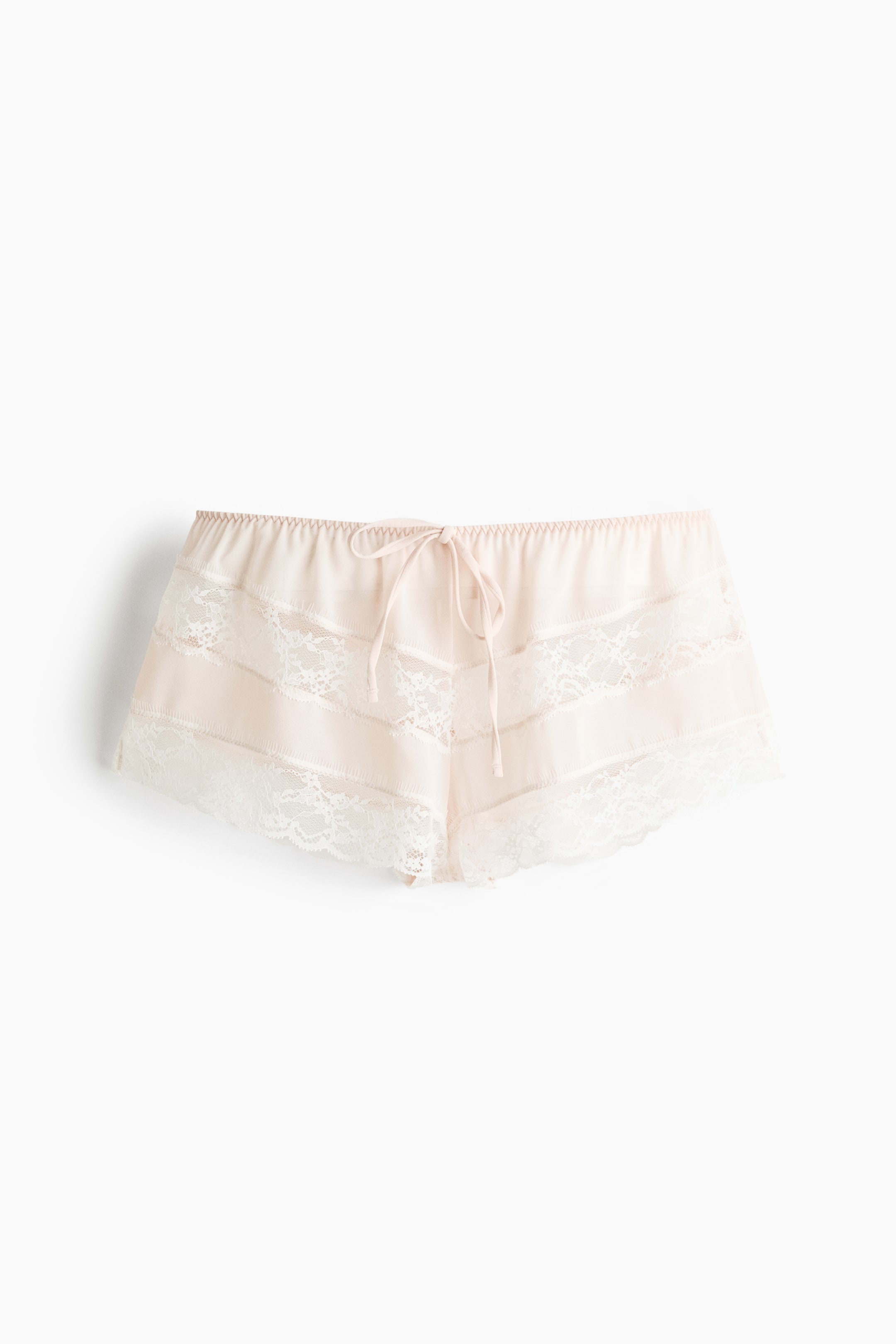 Visa större bild: Ett par ljusrosa shorts med elastisk midja och en volangkant samt en framknuten dragsko. Horisontella vita spetsband pryder framsidan, med matchande spets som kantar bensluten.