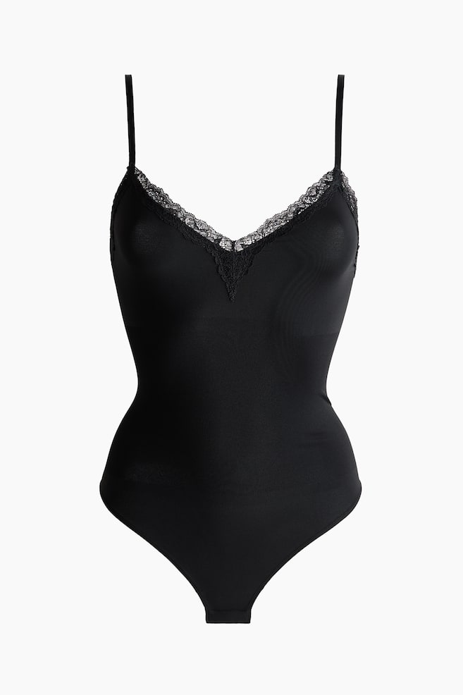 A black bodysuit is displayed front-facing, featuring a V-neckline with delicate black lace trim and slender shoulder straps. It showcases a fitted silhouette, transitioning from a smooth upper section to a subtly ribbed lower torso, and finishes with a thong-style bottom. - 1