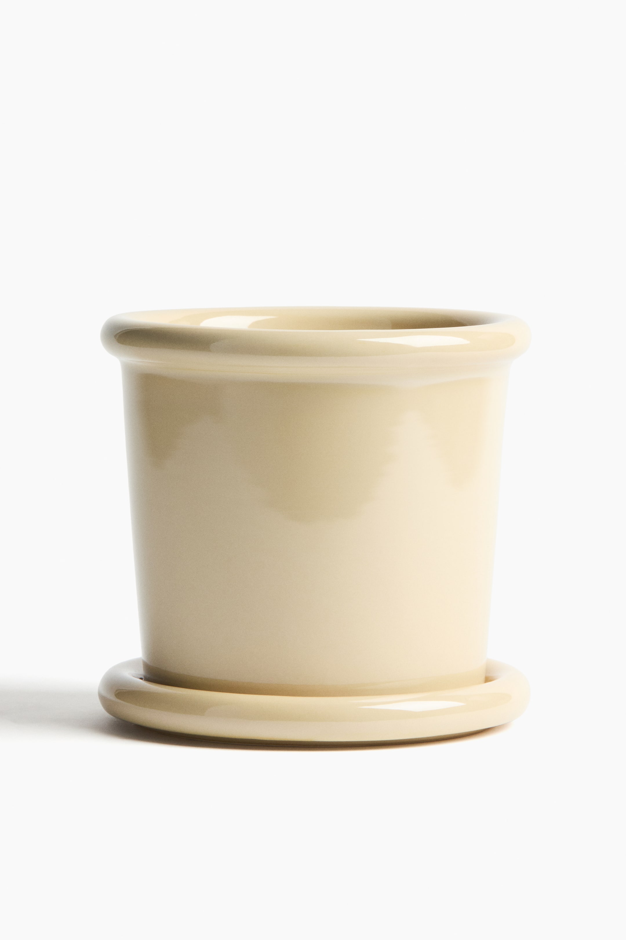 拡大画像を表示: 丸い縁と滑らかなライトクリームの仕上げが特徴の石器製プラントポットが、対応する丸いソーサーの上に置かれています。製品は正面から提示されています。