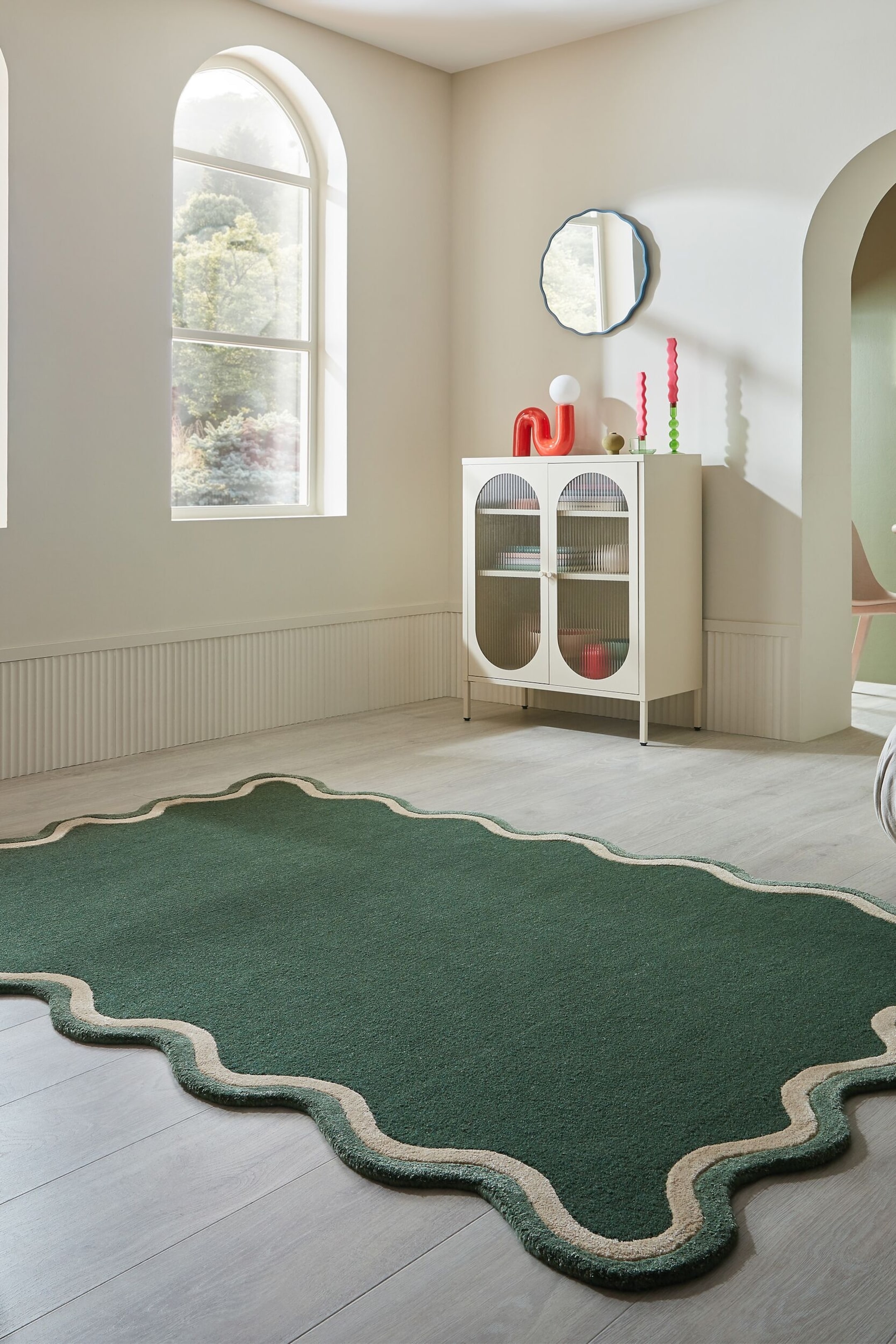 Visa större bild: En mörkgrön matta ligger plant och har en oregelbunden, vågig form med en vågig kant som har en ljusbeige rand på insidan och en mörkgrön ytterkant.