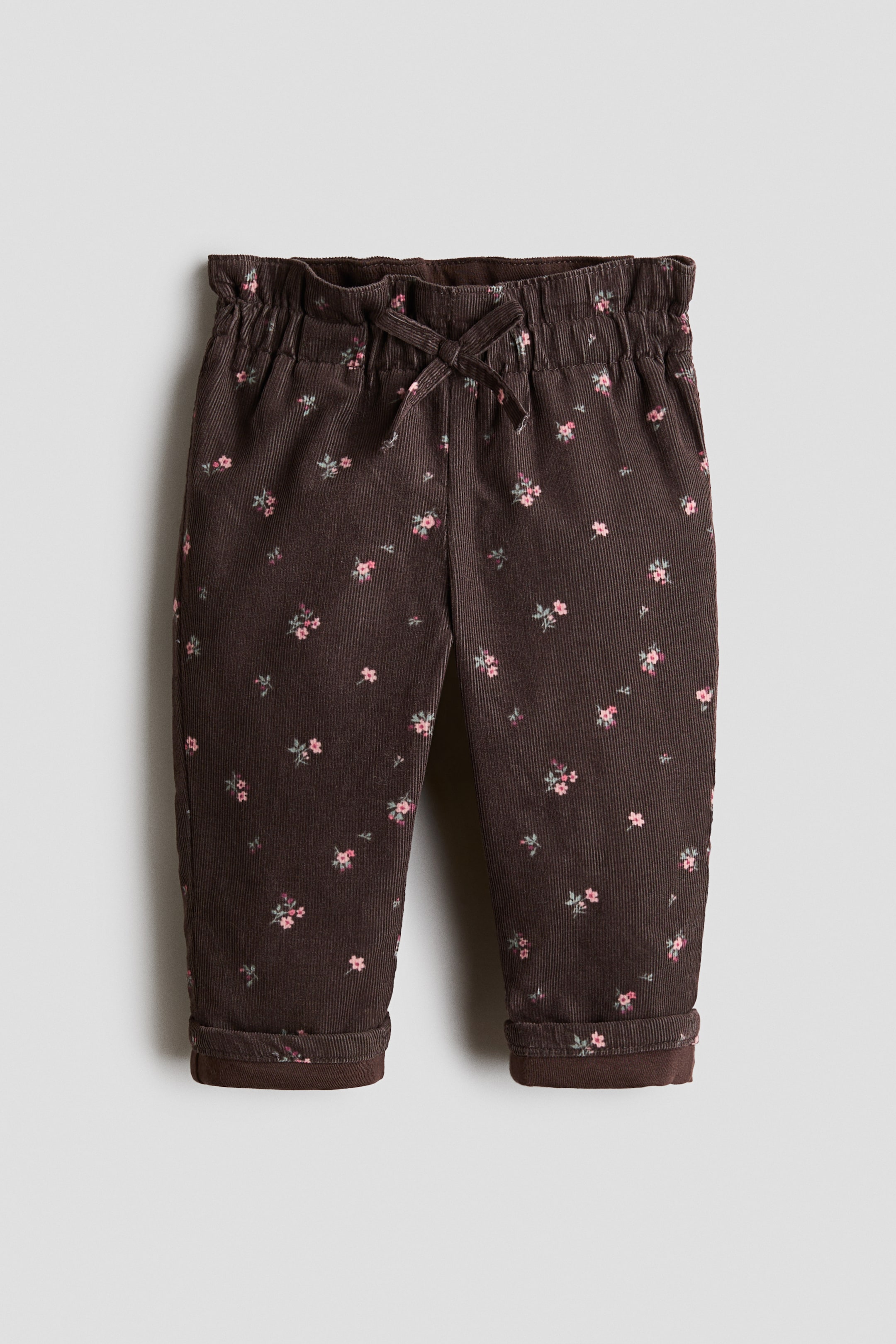 Voir une image plus grande: Le pantalon en velours côtelé brun présente un imprimé floral rose et vert dispersé, une taille élastiquée avec cordon de serrage à l’avant et des revers retroussés.