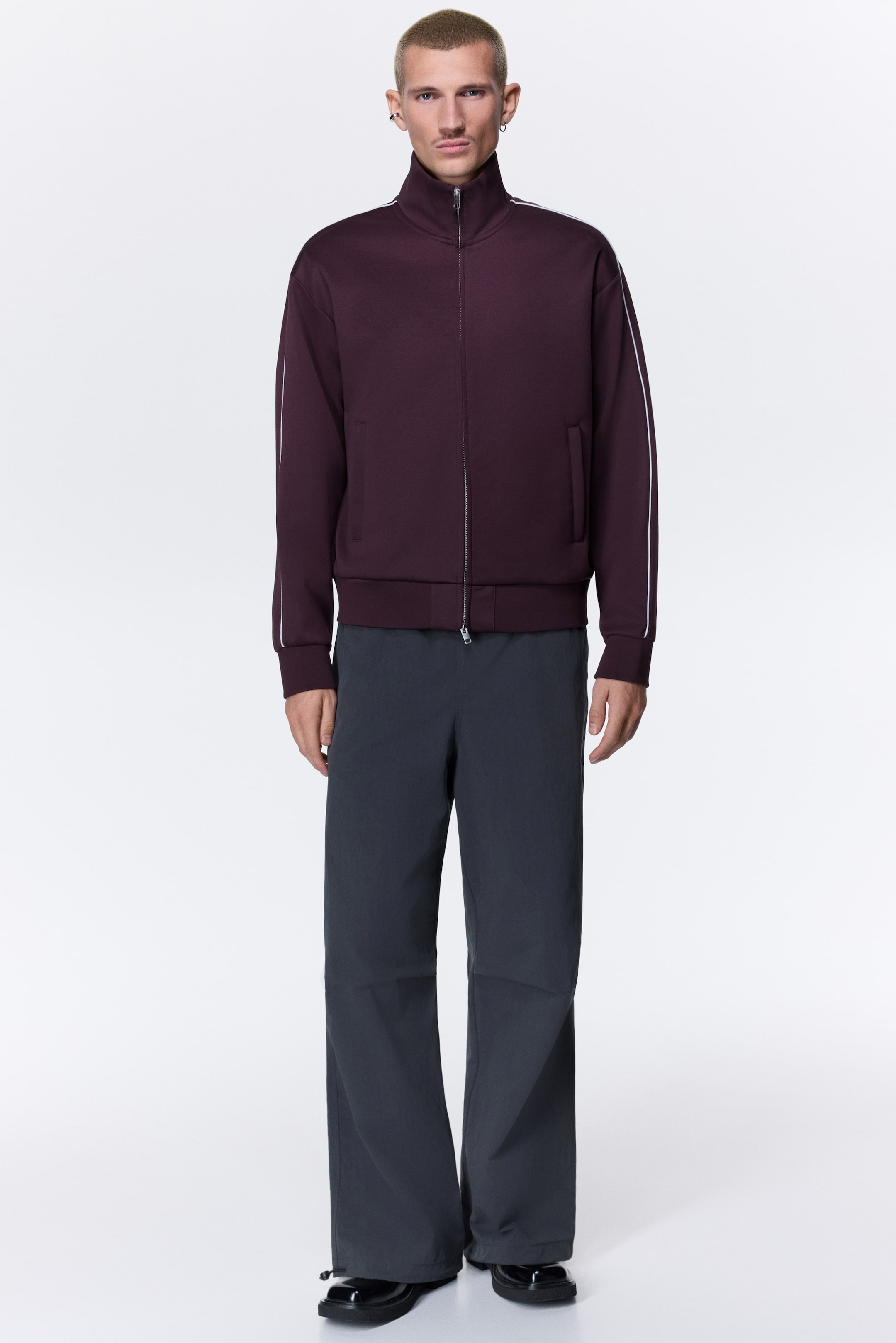 Xem ảnh lớn hơn: Mẫu đang diện chiếc quần màu xám đậm, phom ống rộng với túi xéo hai bên hông. Gấu quần có dây rút kèm chốt khóa, được siết lại ôm quanh đôi giày màu đen.