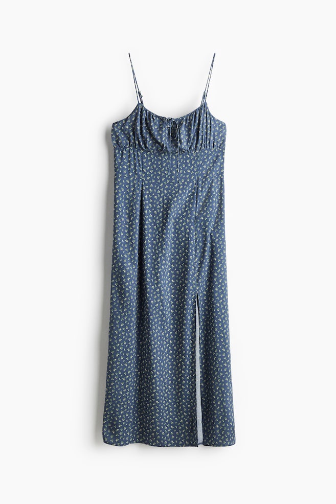 A front-facing blue midi dress is displaying a small floral print, featuring thin spaghetti straps, a ruched bodice with a central tie detail, and a high slit on the left side. - 1