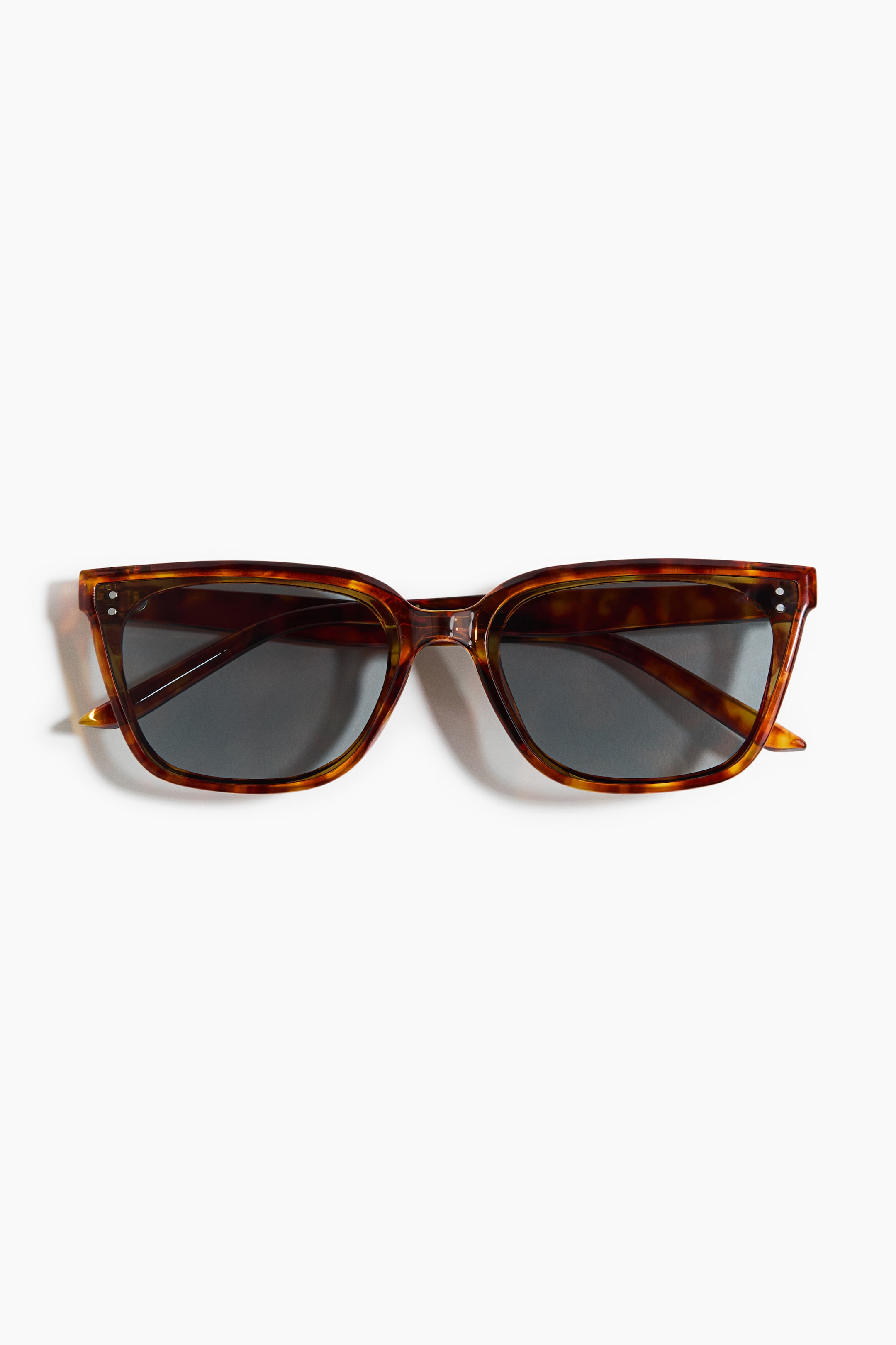 View larger image: The front of the tortoiseshell sunglasses features an angular frame with dark lenses. Small circular silver-coloured accents are visible at the outer corners of the frame.