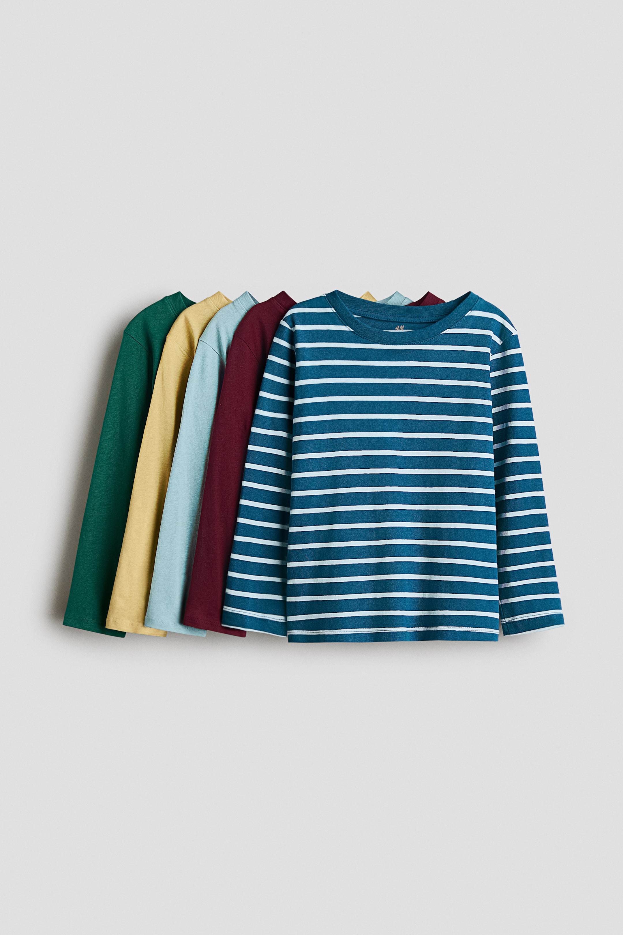 View larger image: Five long-sleeved tops in soft cotton jersey are arranged in a staggered row, each featuring a round neckline with a narrow trim. The frontmost top is shown in teal with white horizontal stripes and faces forward, while four solid-colored tops in burgundy, light blue, yellow, and dark green are partially visible behind it.