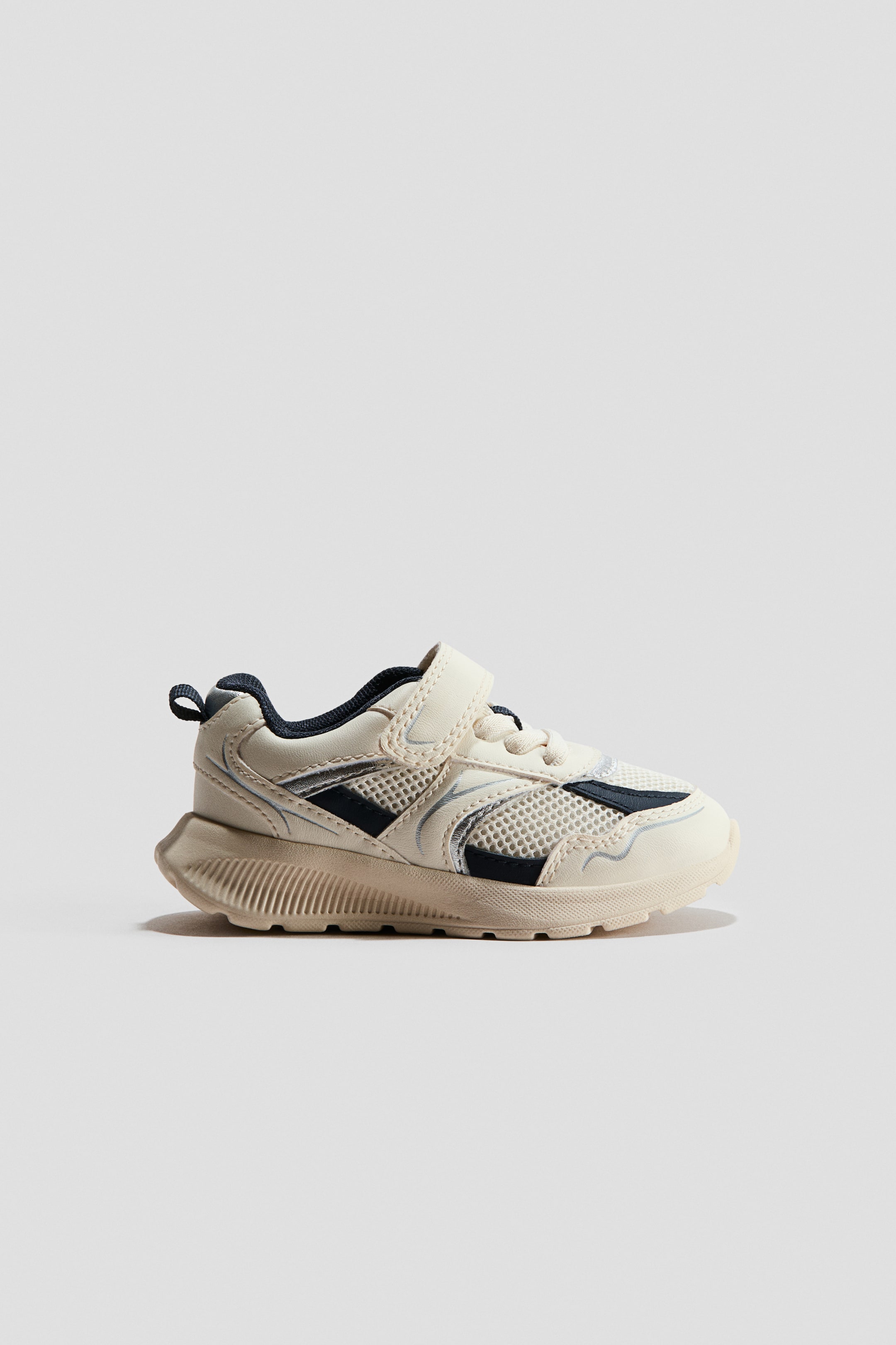 View larger image: The beige sneaker features a mesh upper with dark blue and silver synthetic overlays. It is fitted with a single hook-and-loop strap closure and features a chunky, textured sole.