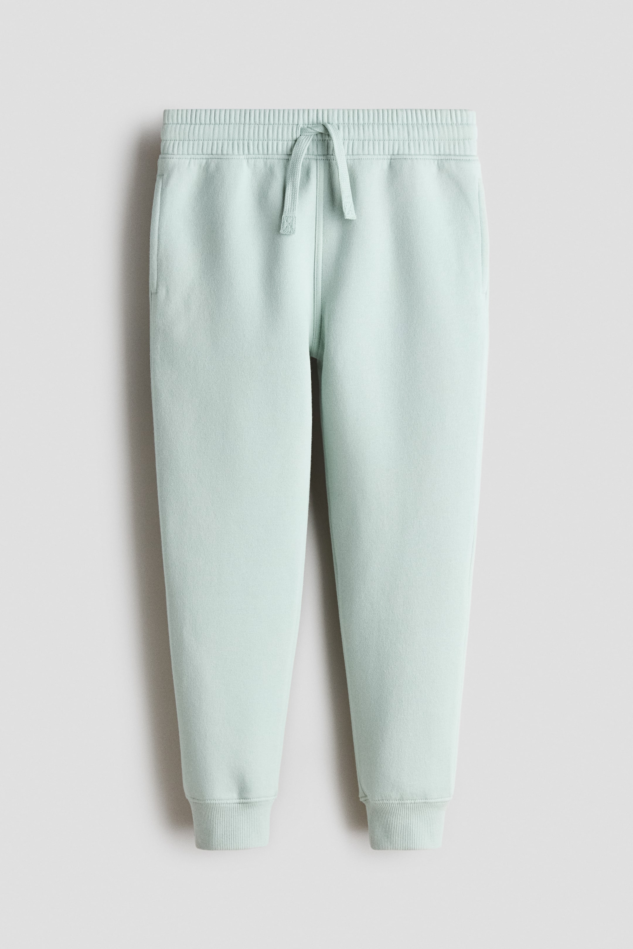 Größeres Bild ansehen: Mintgrüne Jogginghosen aus weichem Sweatshirtstoff präsentieren ihre Vorderseite. Sie verfügen über einen elastischen Kordelzug in der Taille, Seitentaschen und leicht zulaufende Beine, die mit gerippten Bündchen abschließen.