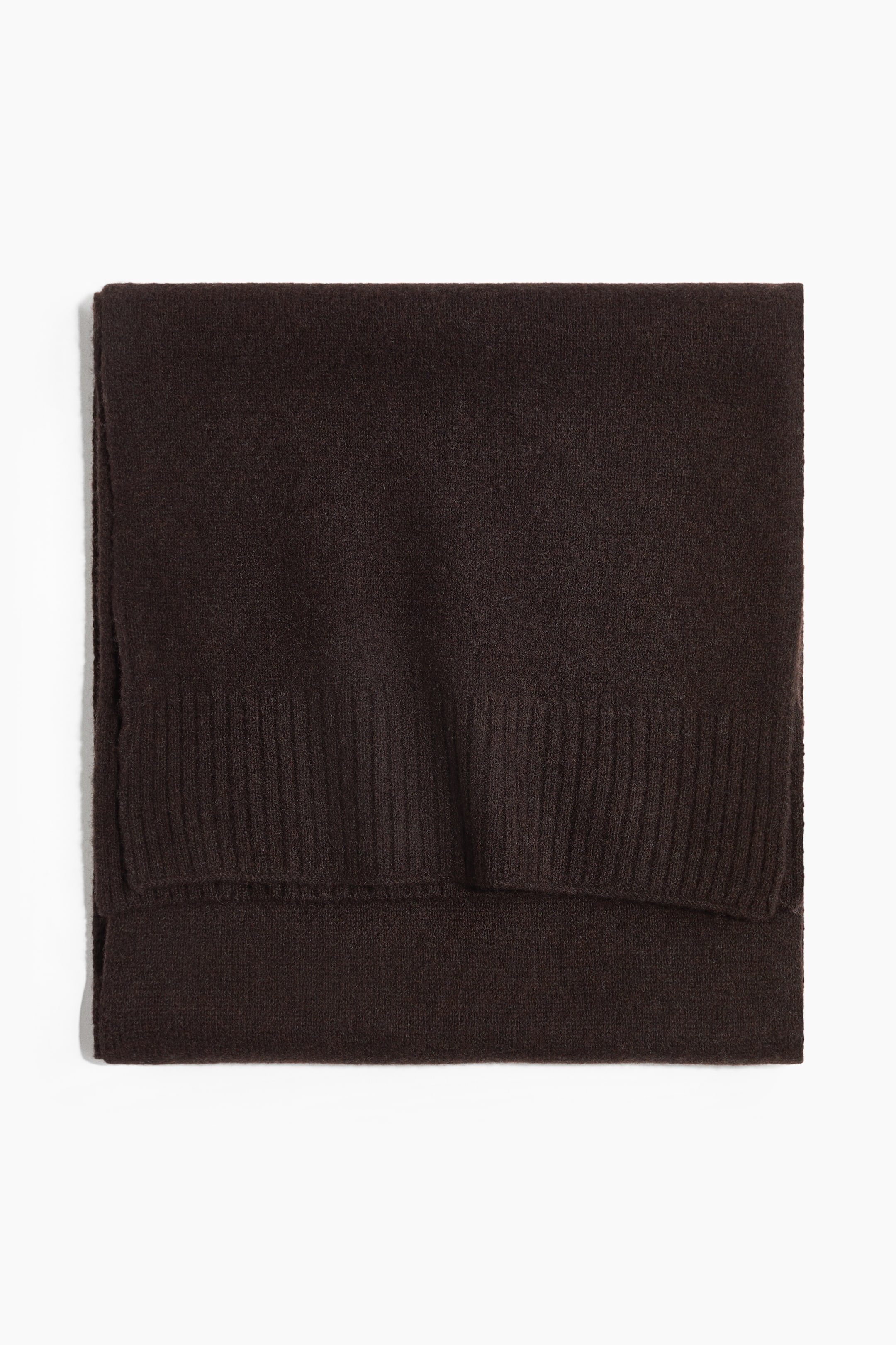 Größeres Bild ansehen: Ein dunkelbrauner Strickschal liegt flach gefaltet und zeigt seine feine Strickstruktur sowie einen breiten Rippensaum am Rand. Das Produkt wird von vorne präsentiert und hebt das weiche Material sowie die saubere, rechteckige Faltung hervor.