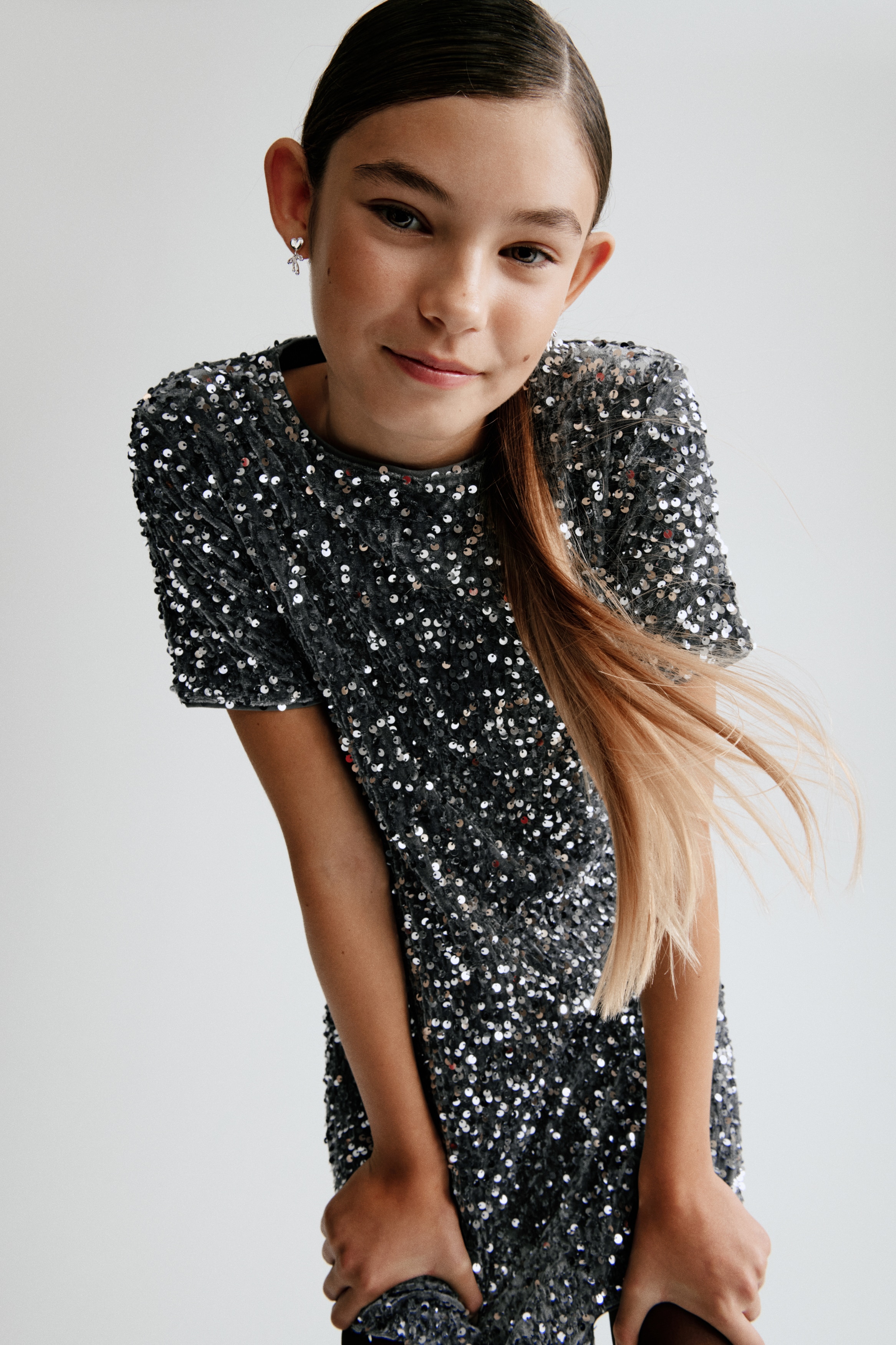 A short-sleeved shift dress in dark grey is facing front, showcasing its all-over embellishment of shimmering silver sequins. The dress features a simple crew neckline and a straight hemline.