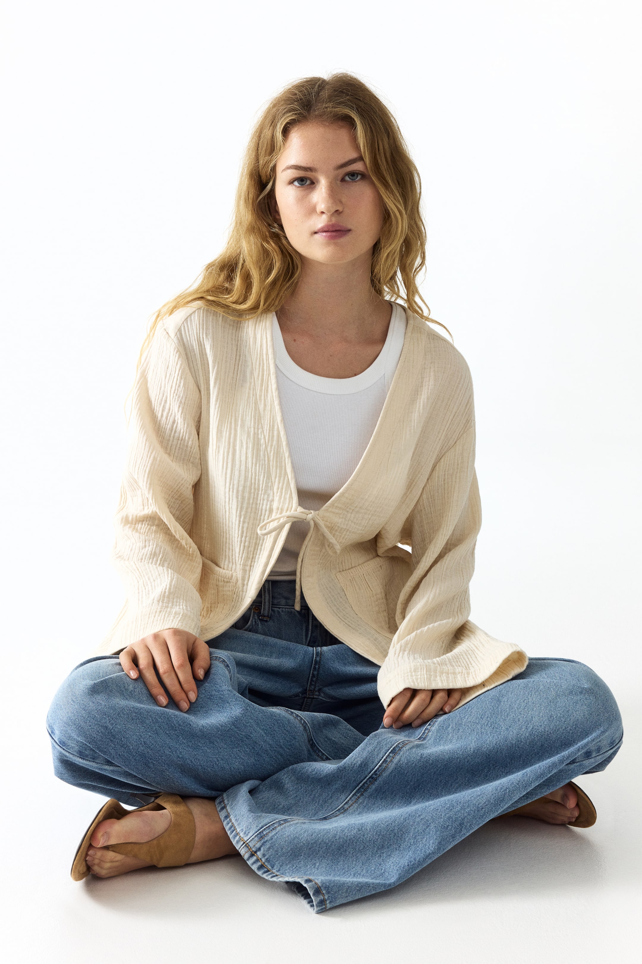 View larger image: A light cream crinkled jacket is worn open over a white ribbed top, featuring a tie closure at the waist and two front patch pockets.