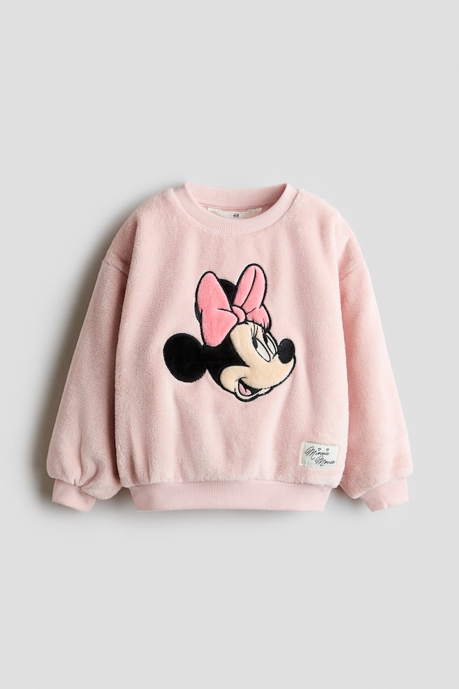 En lyserÃ¸d, blÃ¸d fleece-sweatshirt set forfra med et stort broderet Minnie Mouse-patch midt pÃ¥ brystet. Sweatshirten har en ribstrikket rund hals, sÃ¦nkede skuldre med ribstrikkede manchetter, en ribstrikket kant samt et lille hvidt vÃ¦vet label nÃ¦r nederste kant. - 1