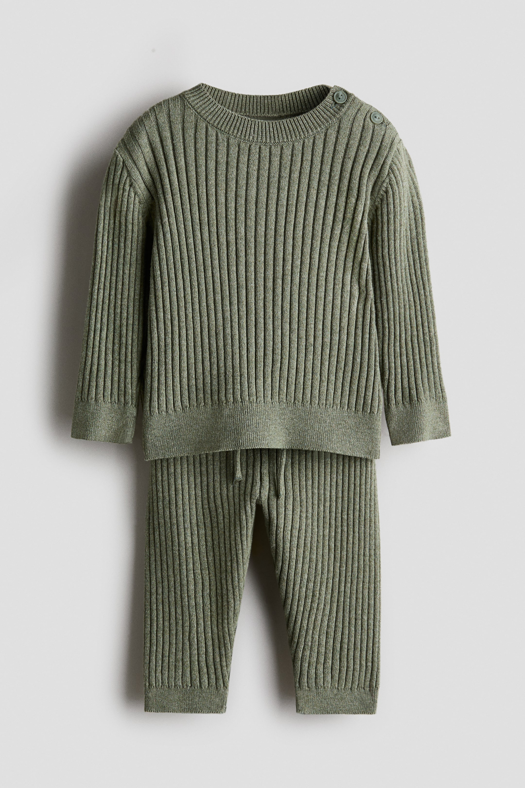 Visualizza l'immagine ingrandita: Un set in maglia a coste larghe verde composto da un maglione e pantaloni, entrambi caratterizzati da una texture a coste larghe. Il maglione presenta due bottoni sulla spalla sinistra e bordi finemente a coste allo scollo, ai polsini e all'orlo, mentre i pantaloni mostrano una vita con coulisse e orli finemente a coste.