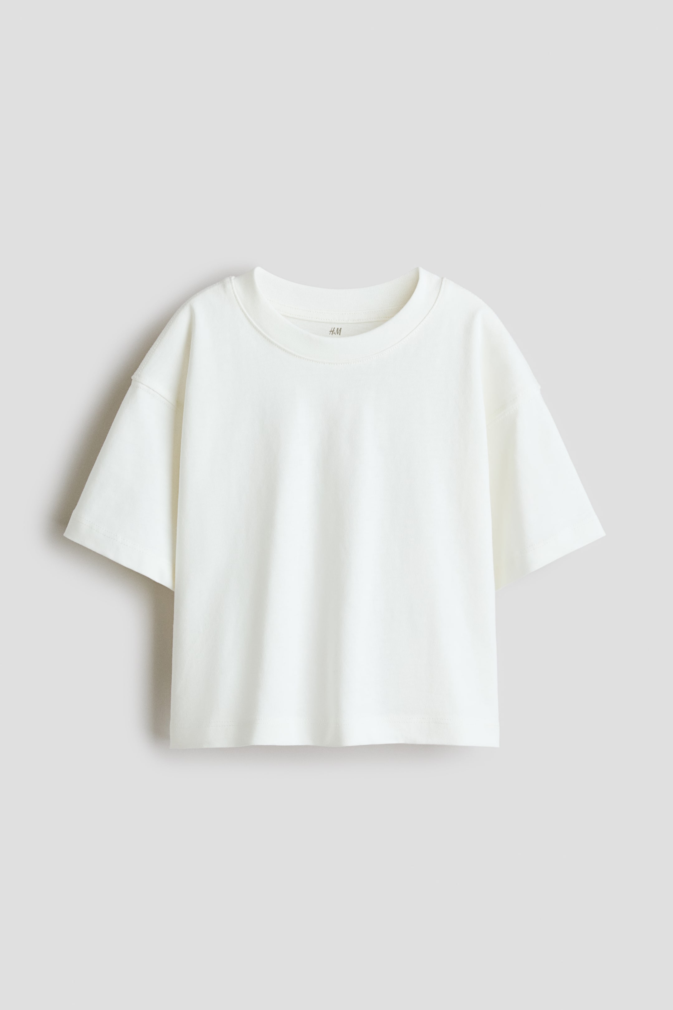 View larger image: A cream t-shirt is displaying its FRONT, featuring a ribbed round neckline and dropped shoulders with wide short sleeves. The H&M brand tag is visible on the inside of the neck, and the shirt is finishing with a straight hem.