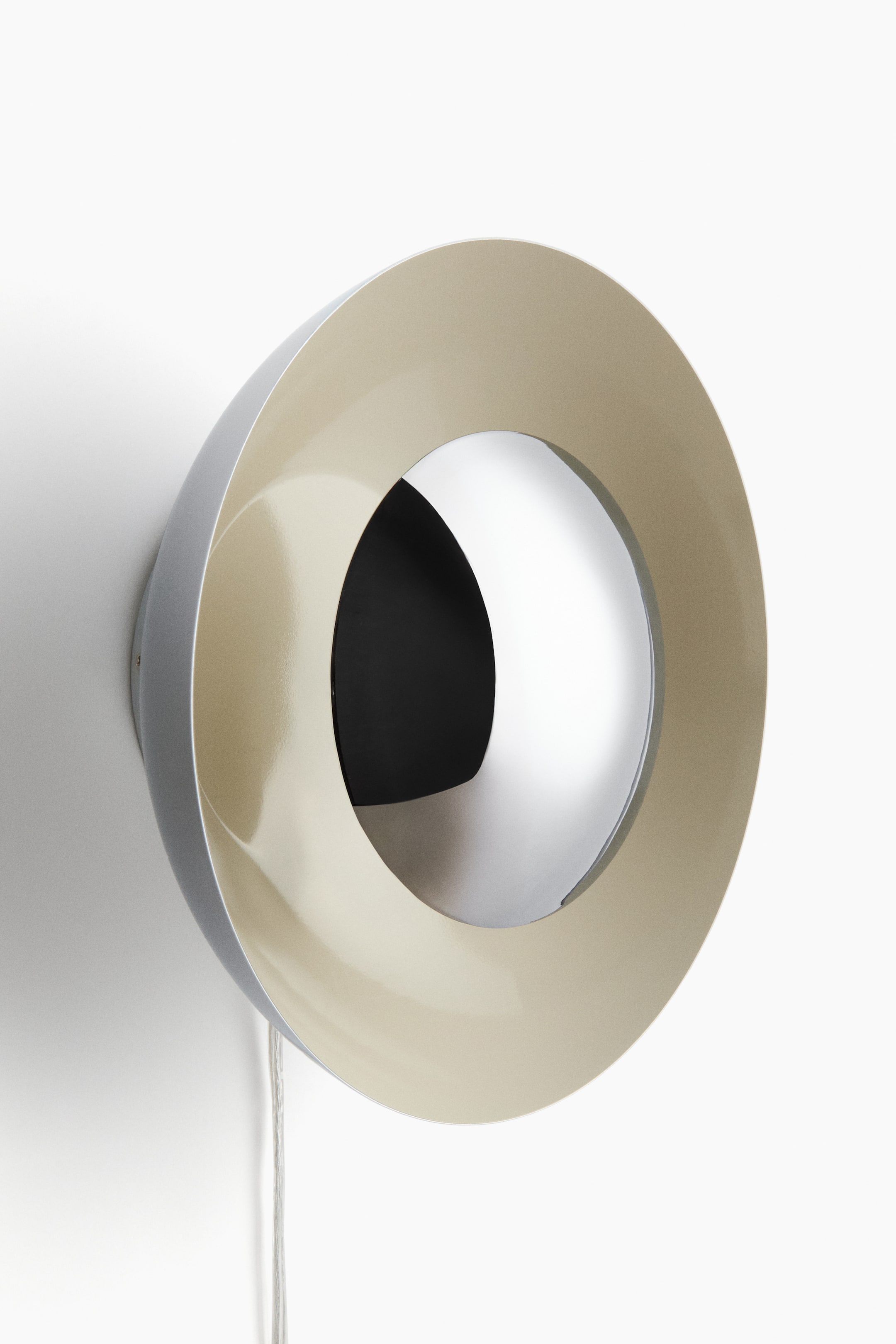 View larger image: A wall-mounted light fitting featuring a multi-layered, circular design, viewed from a slight angle. The fitting's outer casing is a matte silver-grey, and the inner surface of its front ring is a glossy beige. A highly reflective, curved chrome element is recessed into the central opening, with a deep black interior visible behind it, and a white electrical cord extends from the bottom.