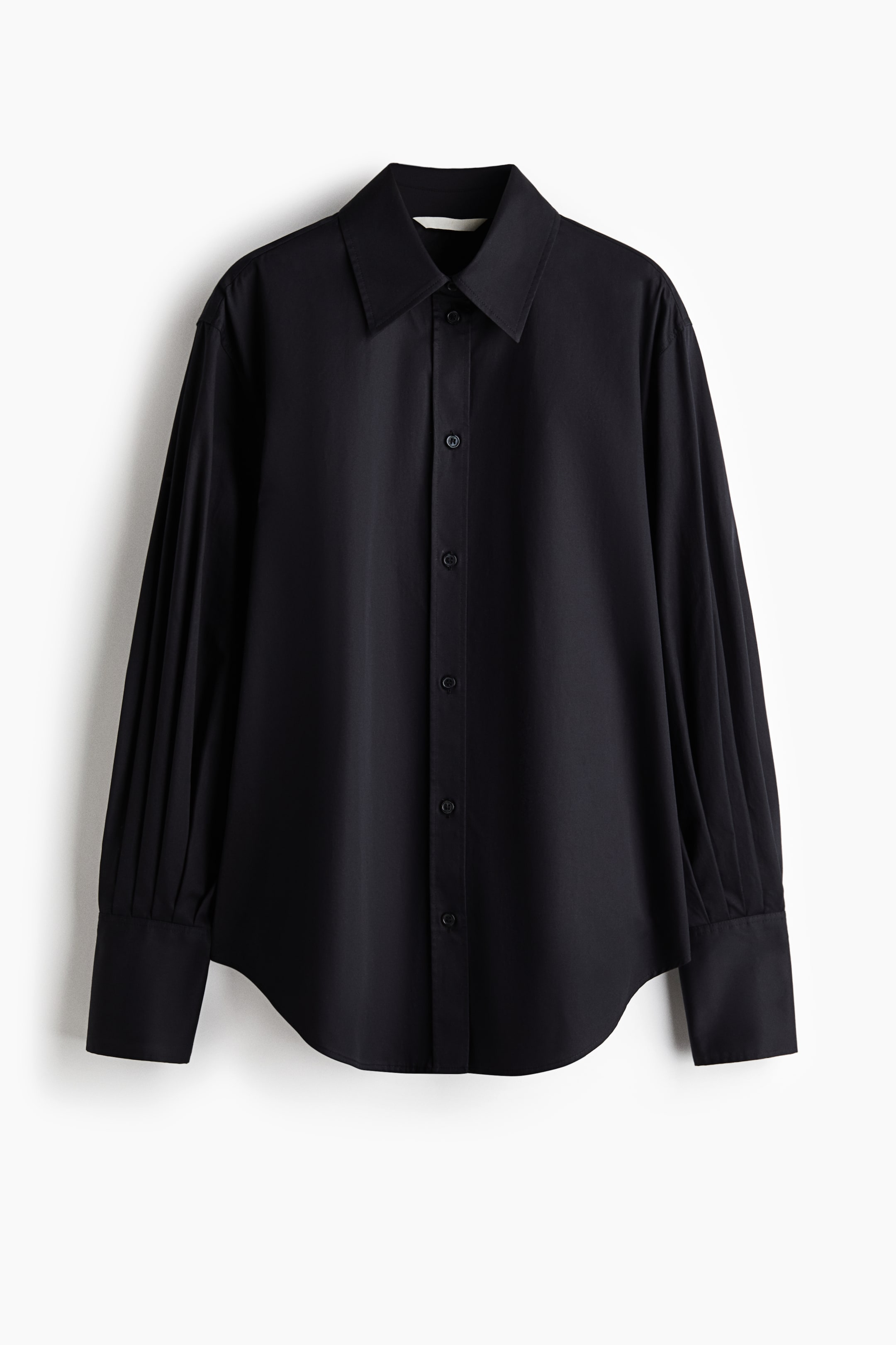 Ampliar la imagen: Vista frontal de una camisa negra abotonada que muestra un cuello clásico con punta, cierre frontal con botones y un dobladillo curvo. Las mangas largas presentan un distintivo pliegue vertical que cae hasta puños anchos y estructurados.