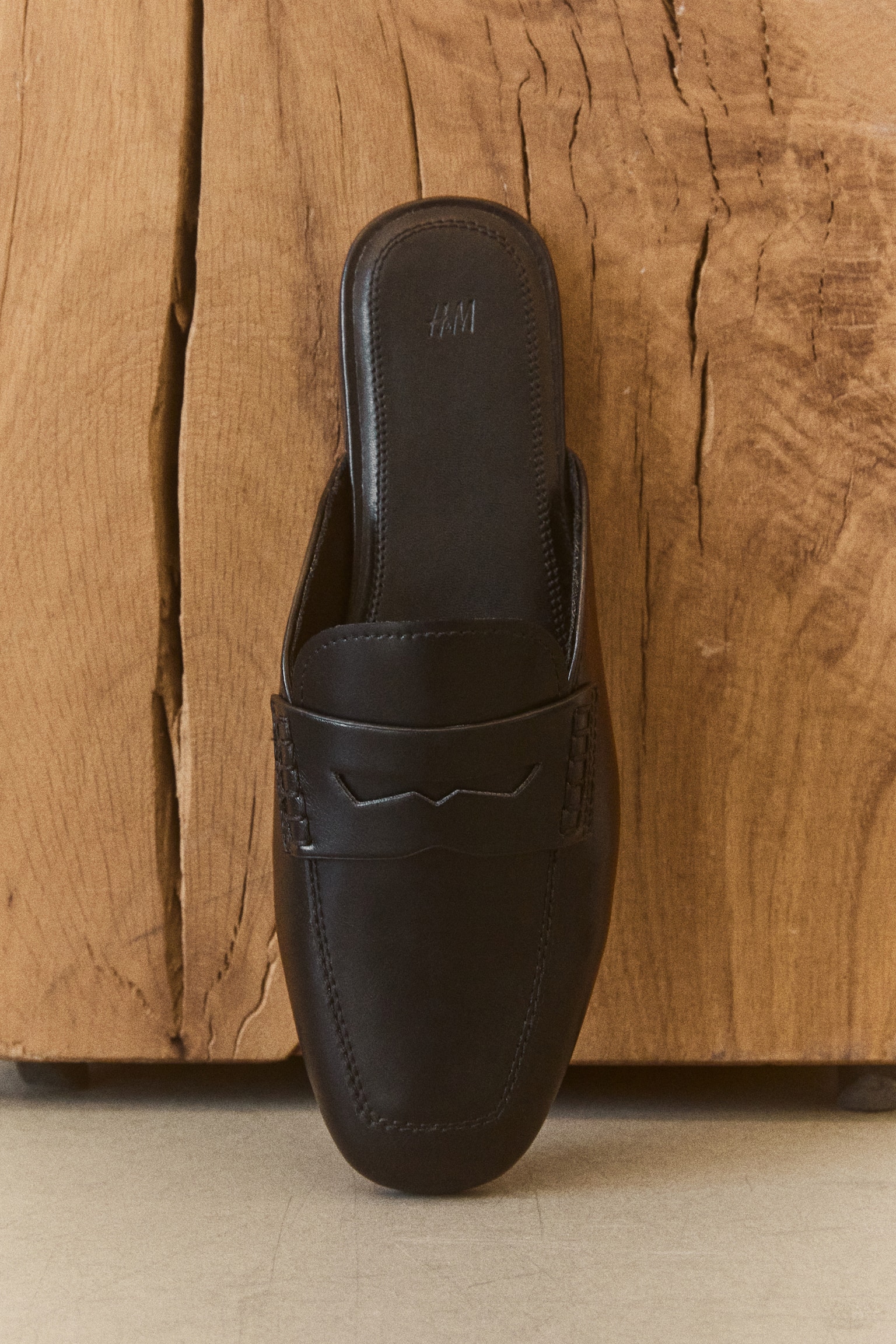 Two black loafer mules are positioned forward, each boasting a sleek finish, a slightly square toe, and a timeless loafer design. A saddle strap with a decorative cut-out graces the instep, while visible stitching accents the toe box. The H&M logo is embossed on the black insole of each shoe. - 1