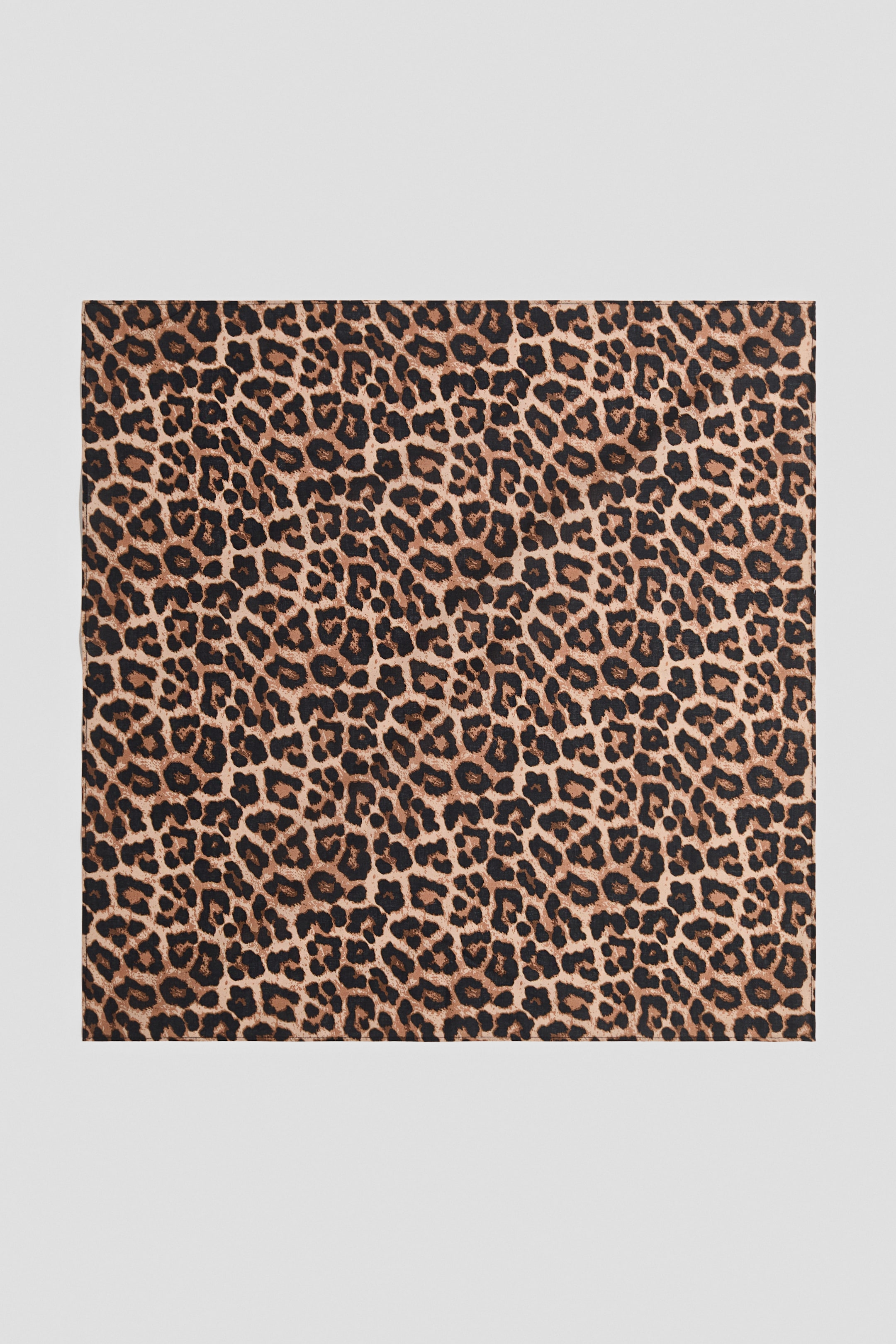 Se større billede: Det rektangulære stof har et leopardprintmønster med uregelmæssige sorte og mørkebrune pletter på en lysebrun baggrund.