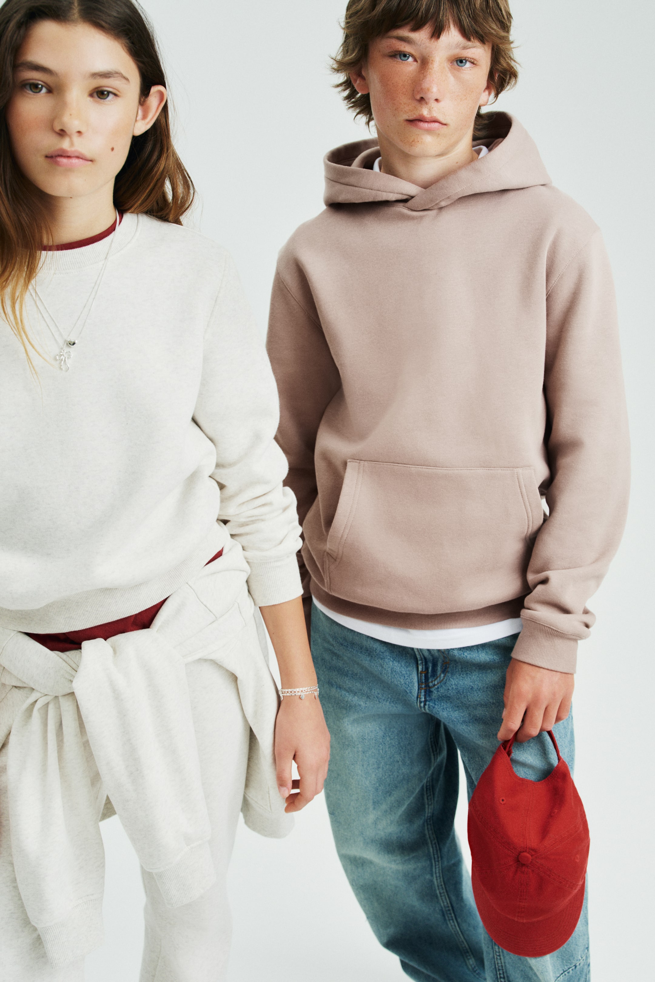 View larger image: A light brown hoodie made of sweatshirt fabric is showcased from the front, featuring a jersey-lined hood with a wrapover front, subtly dropped shoulders, and long sleeves. It includes a kangaroo pocket and ribbed cuffs and hem, with a white t-shirt peeking out from underneath the hem.