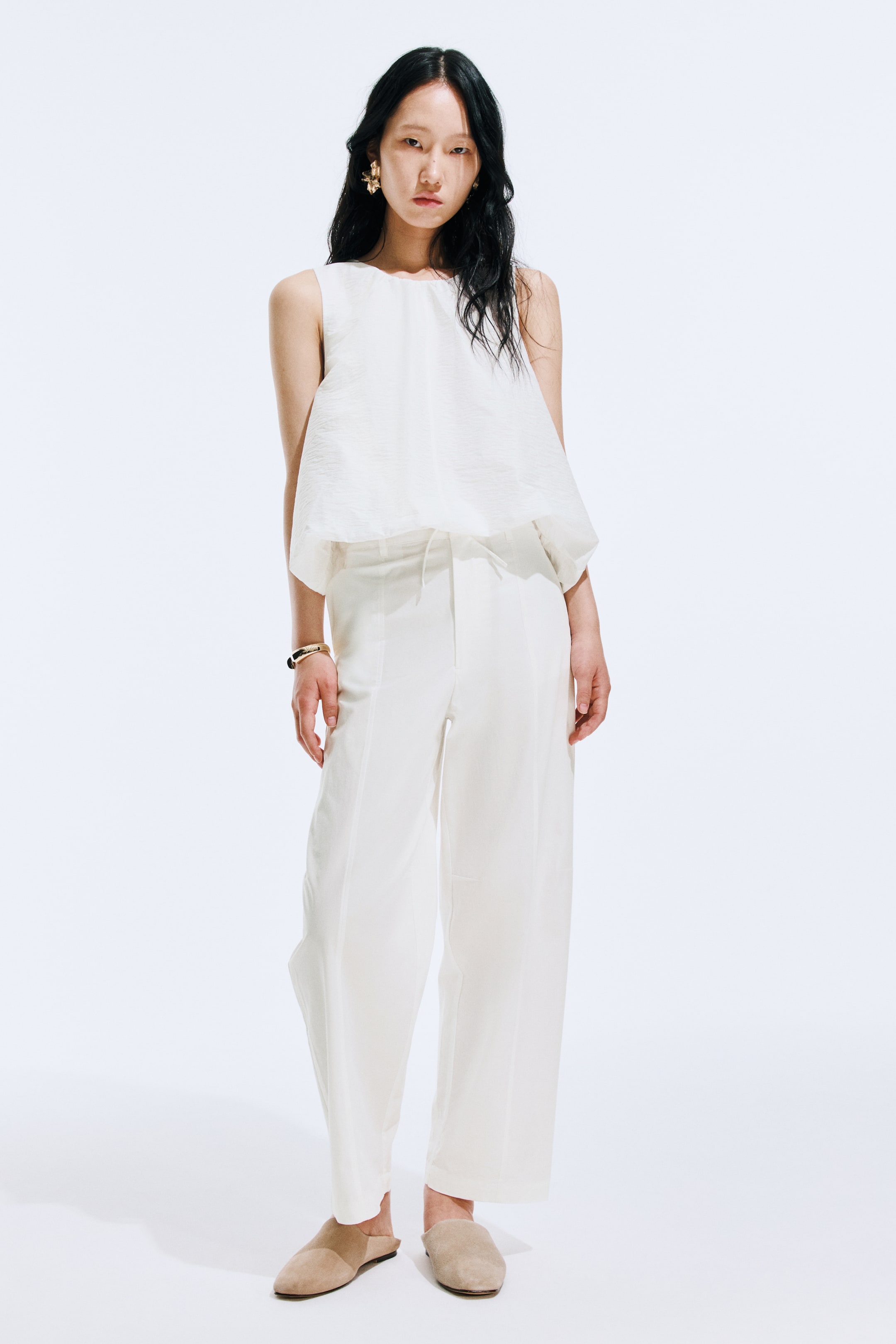 View larger image: "Light-colored, relaxed-fit trousers featuring a baggy silhouette and prominent seams running down the front of the legs are showcased by the model."