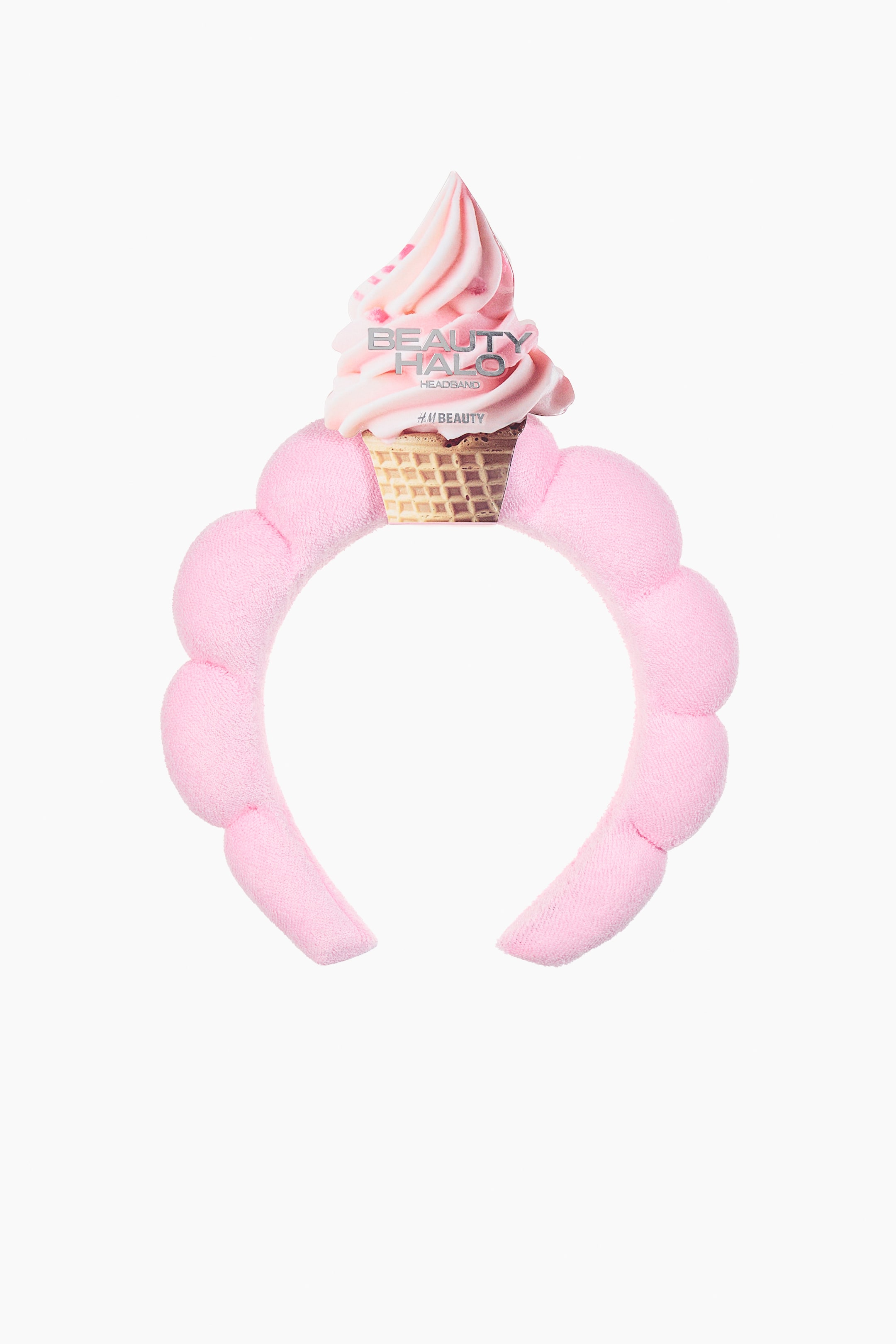 Ampliar la imagen: Una diadema acolchada rosa, hecha de tela suave, presenta una forma festoneada con secciones redondeadas distintas que forman la banda. Una etiqueta diseñada como un cono de helado suave rosa está adherida en el centro superior, mostrando "Beauty Halo Headband".
