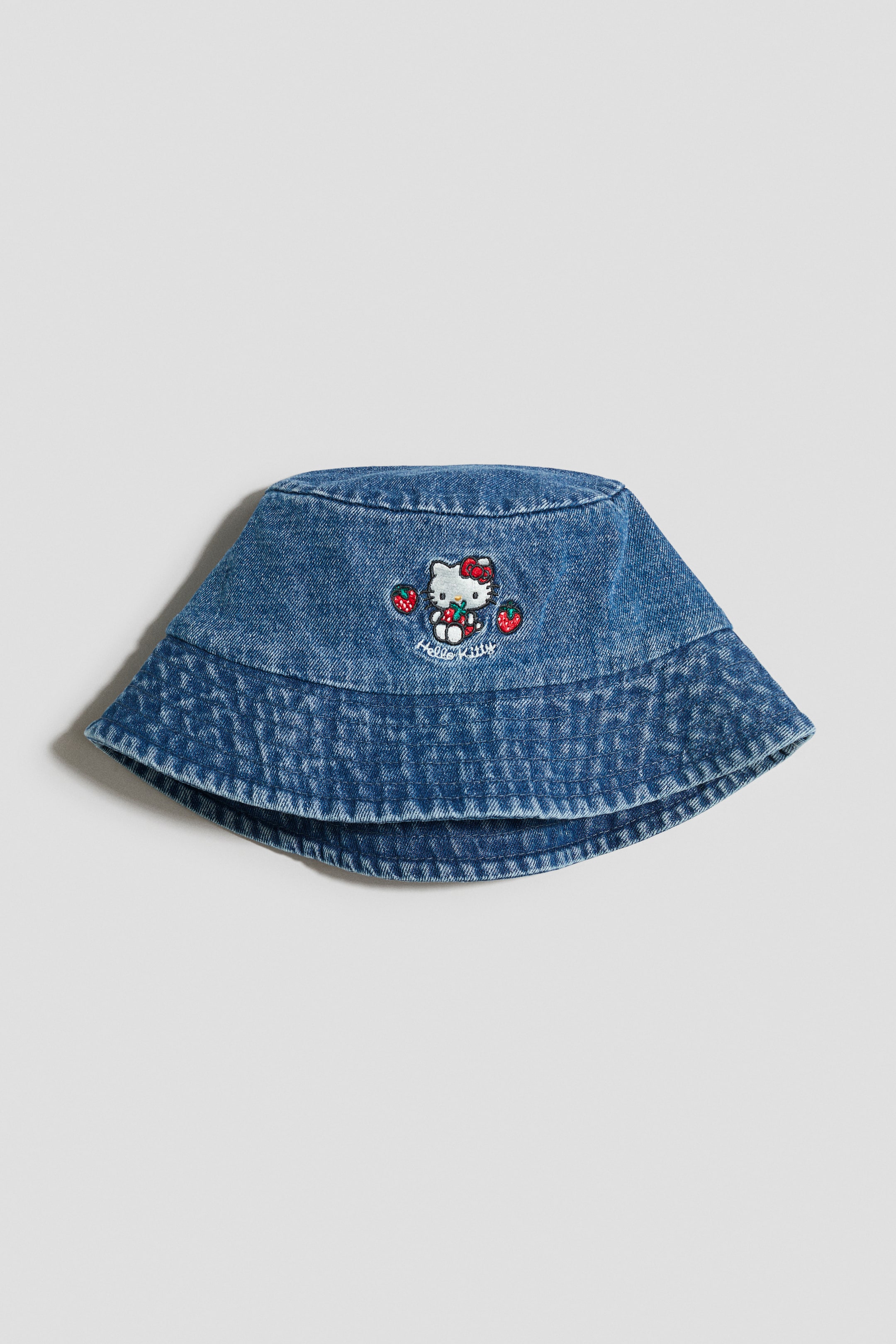 View larger image: A blue denim bucket hat is showcased at the front, featuring an embroidered Hello Kitty design holding strawberries, with additional strawberries on each side and 'Hello Kitty' text beneath the character.