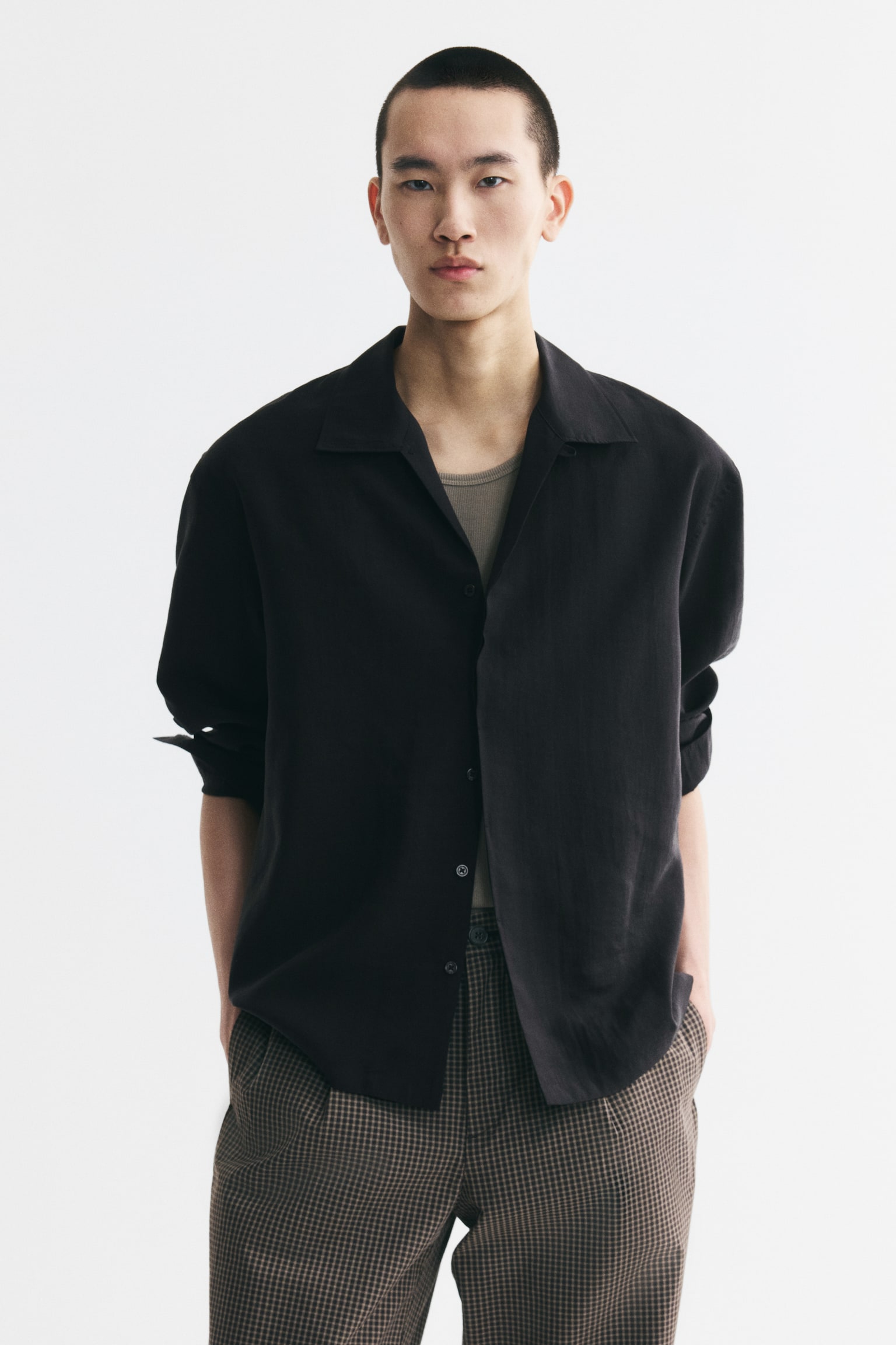A black long-sleeved shirt is laid flat, showcasing its front side. It features an open revere collar forming a V-neckline, and long sleeves with simple cuffs. - 1