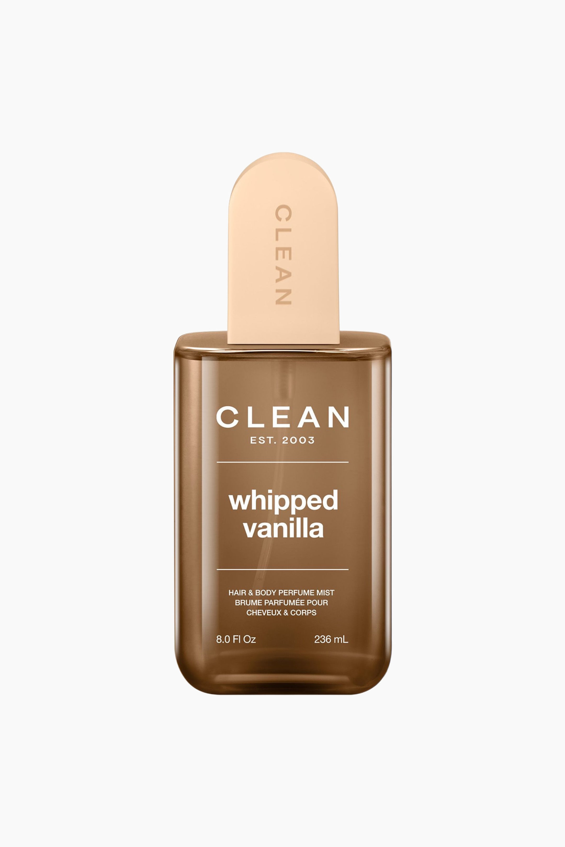 Se større billede: En gennemsigtig brun rektangulær flaske med Clean Whipped Vanilla Hair & Body Perfume Mist står oprejst, vendt fremad, med en lys beige, buet hætte, der viser "CLEAN" lodret, og flaskens forsideetiket, der detaljerer produktets navn, type og volumen i hvid tekst.