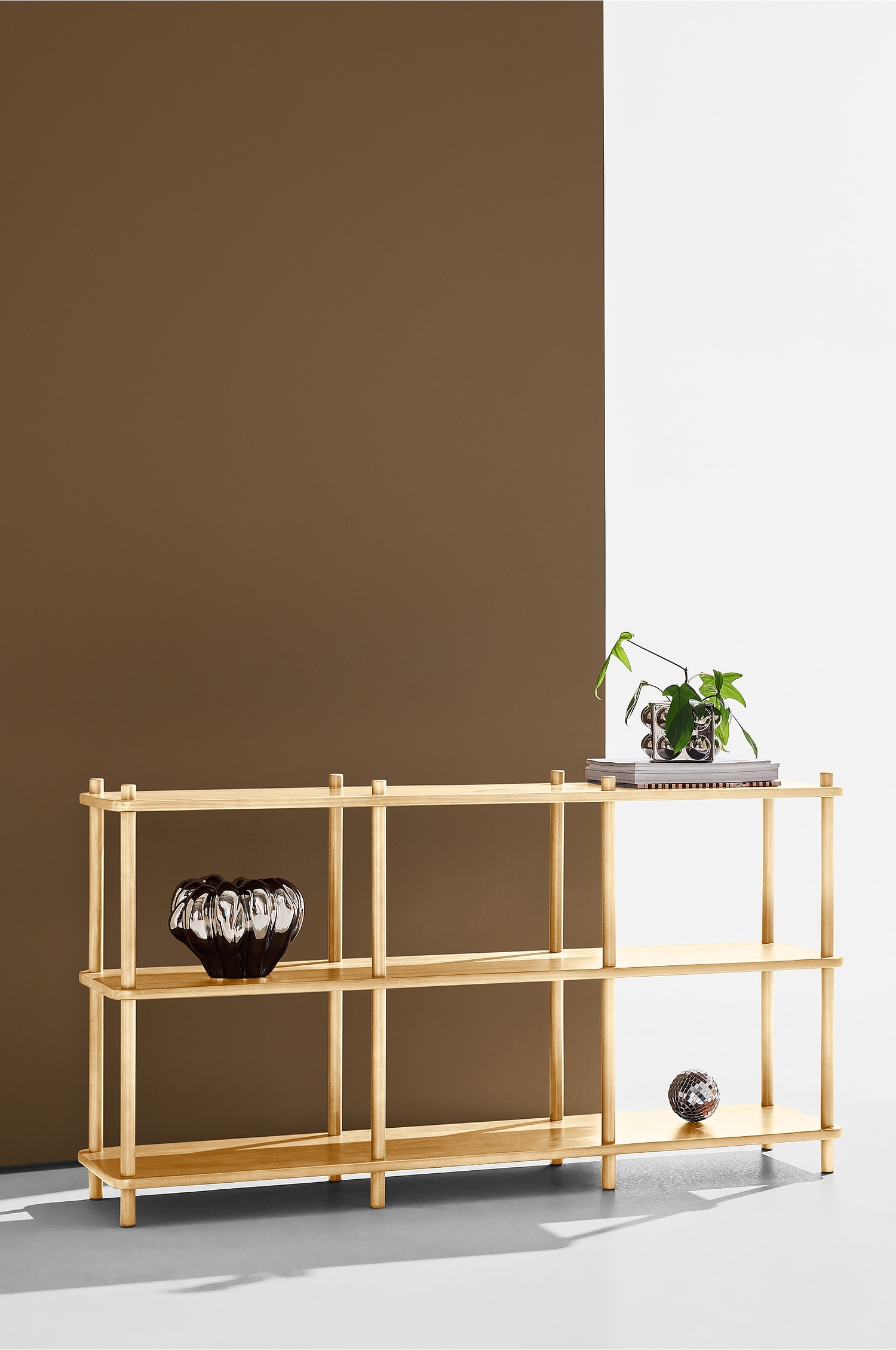 Ein helles Holzregal steht in einer Dreiviertelansicht und präsentiert ein offenes Design mit drei horizontalen Einlegeböden. Die Struktur wird von runden, vertikalen Pfosten getragen, die das Regal in drei Spalten unterteilen und leicht über das obere Regalbrett hinausragen.