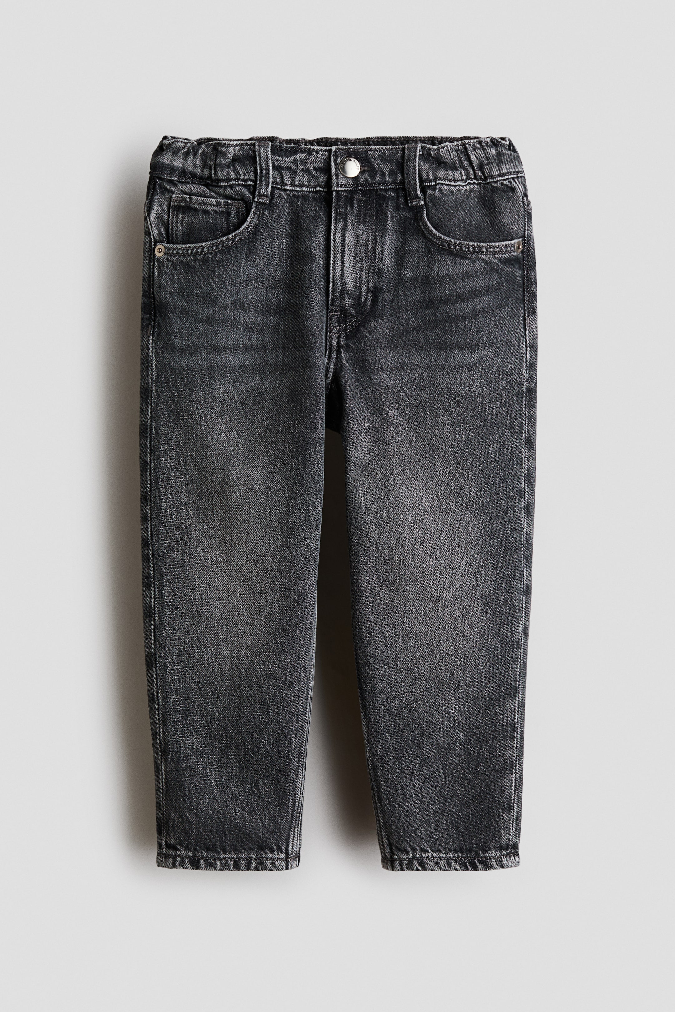 Vis større bilde: Mørkegrå denimjeans vises forfra, med en elastisk midje med beltehemper og en enkelt sølvknapp. De har to avrundede frontlommer og ben som smalner forsiktig.